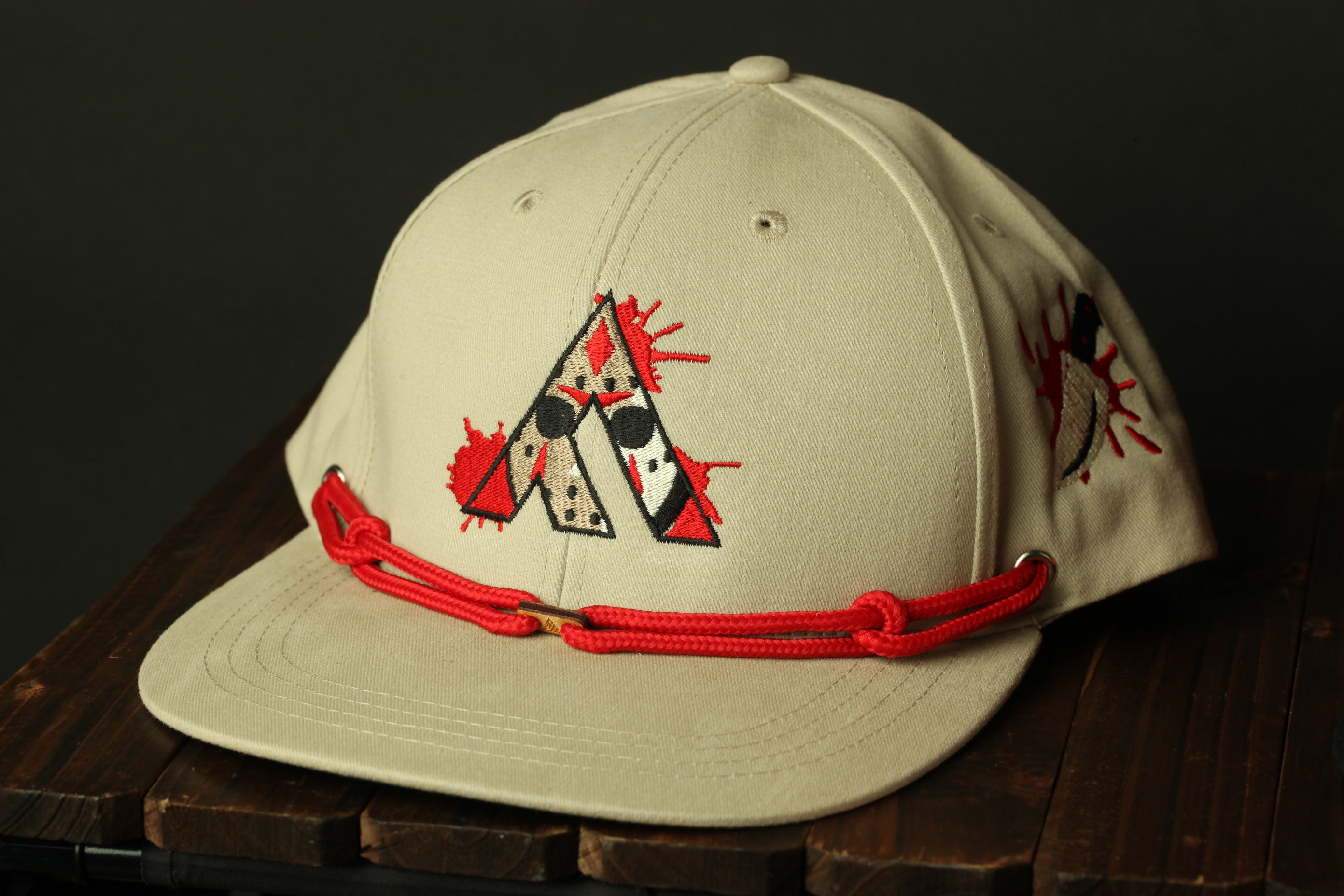 A beige baseball cap with a red string and a graphic design on the front, placed on a wooden surface.