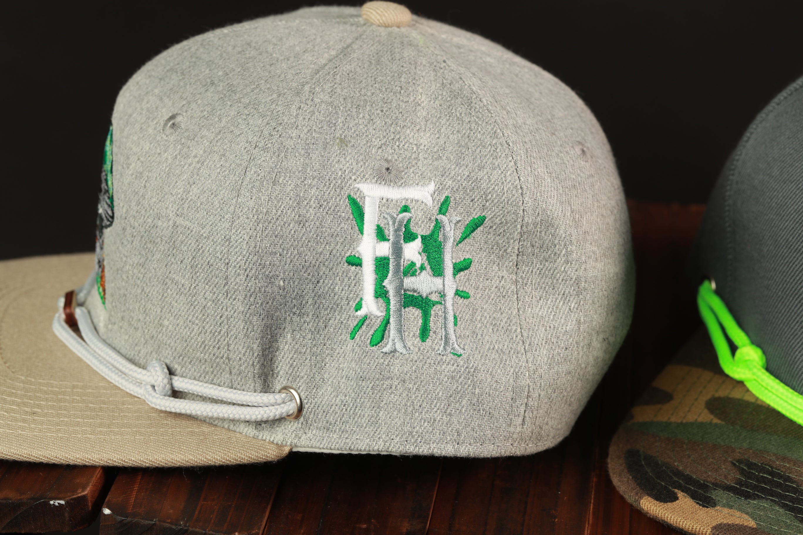 a gray baseball cap with a green and white embroidered logo on the front, placed on a wooden surface.