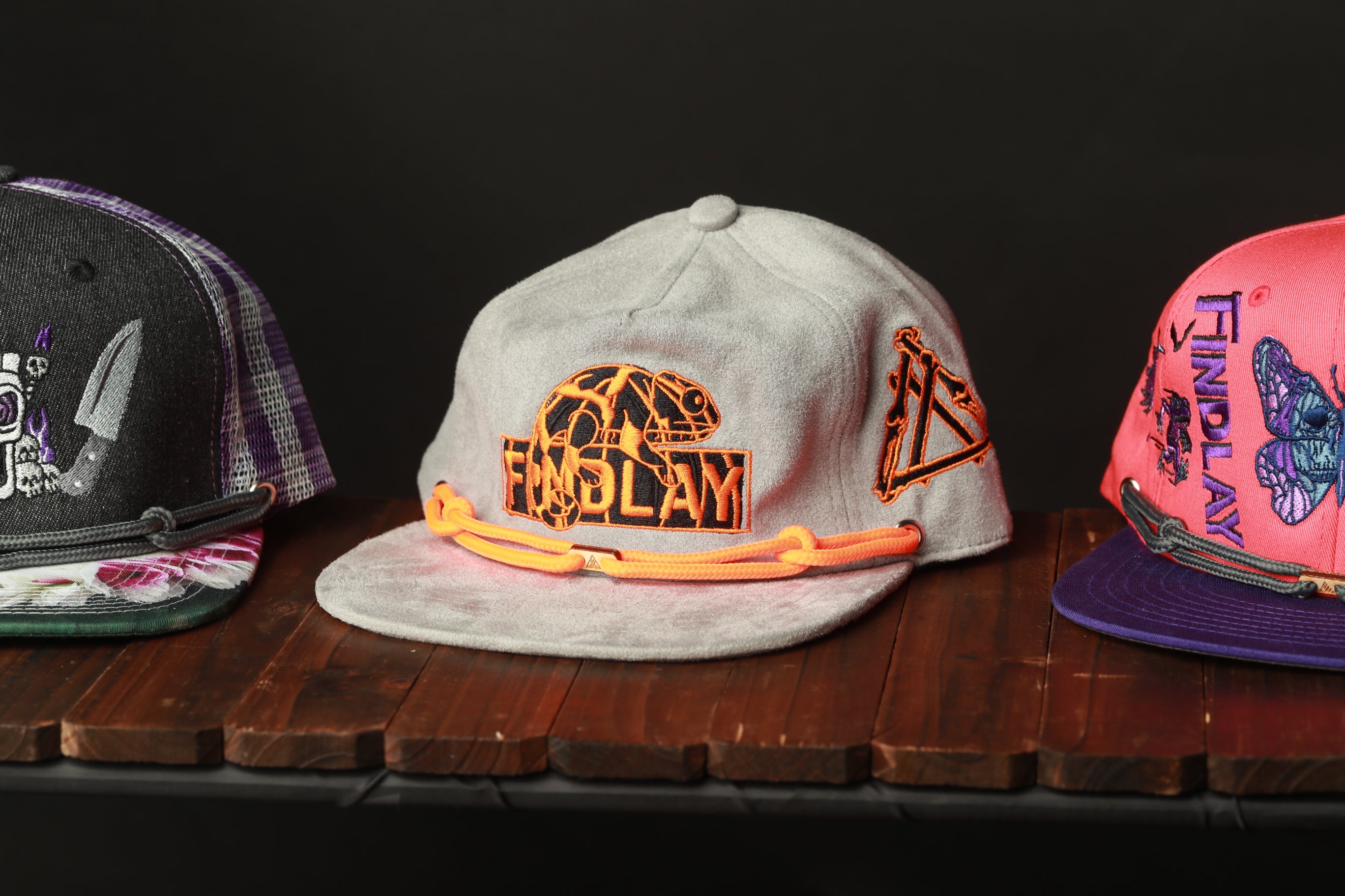 Three baseball caps are displayed on a wooden surface, each with unique designs and colors.