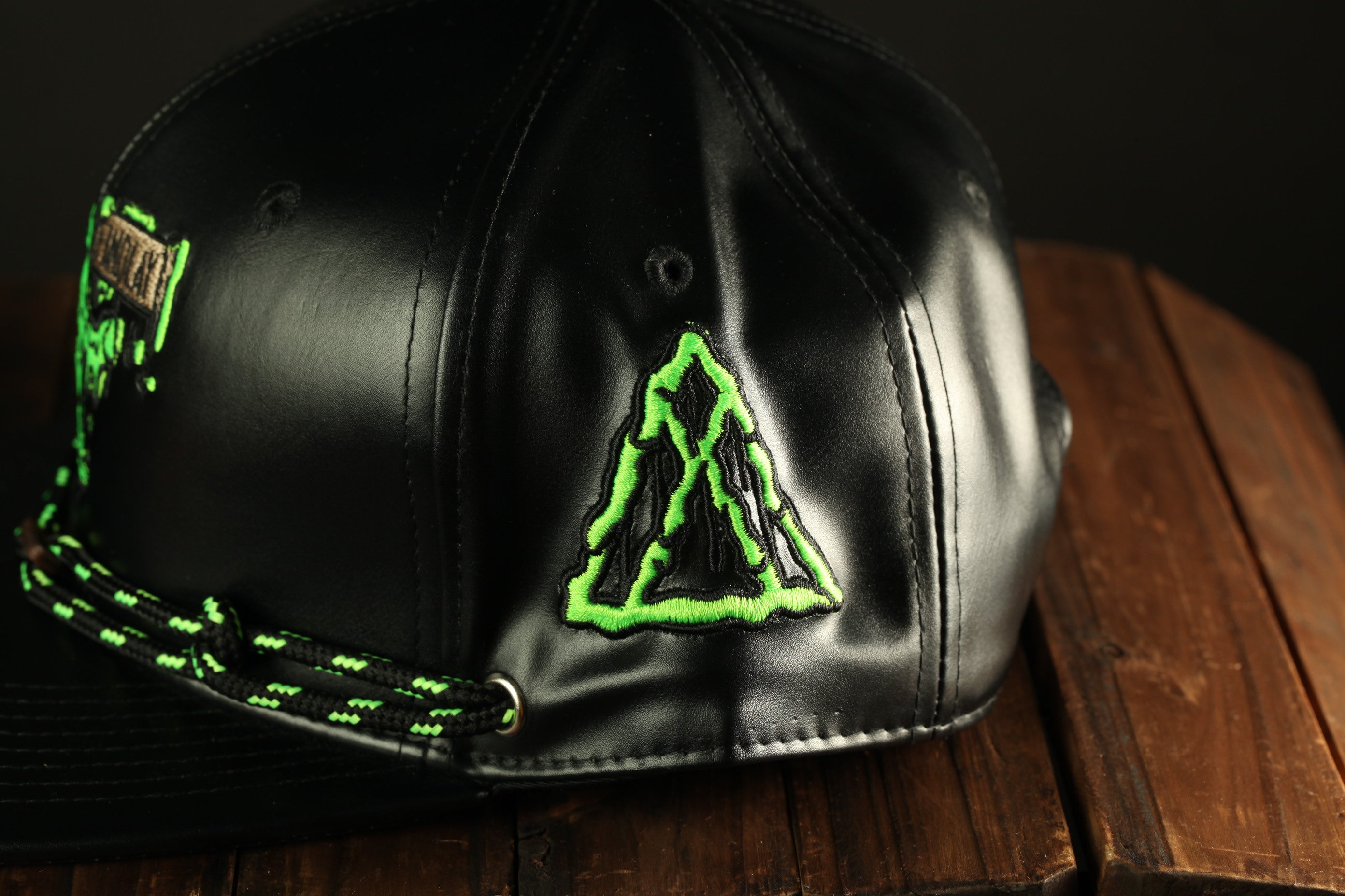 A black baseball cap with a green triangle design on the front, placed on a wooden surface.