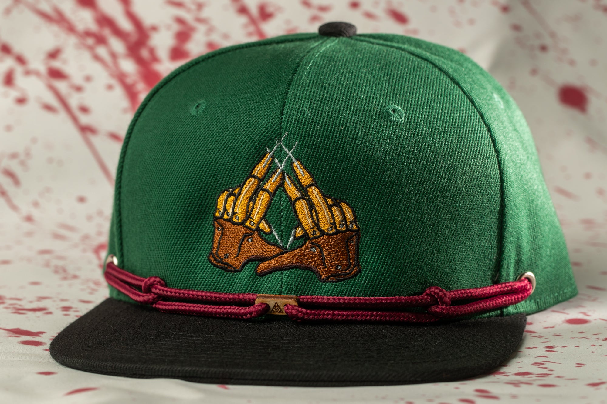 A green baseball cap with a graphic design on the front, featuring a pair of hands with a claw-like appearance.