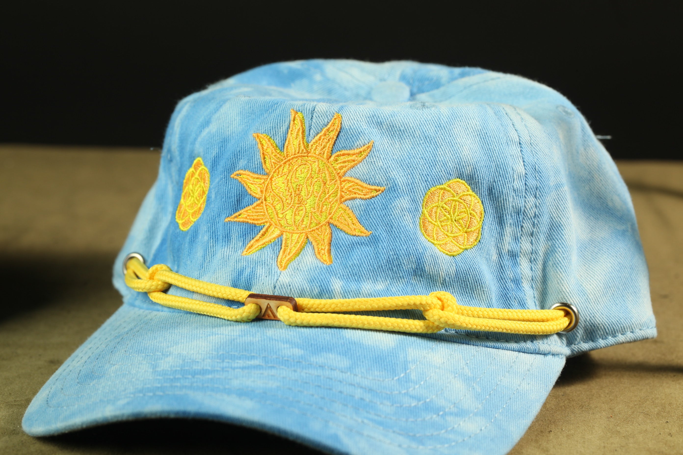 A blue baseball cap with yellow sun embroidery and a yellow chain strap.
