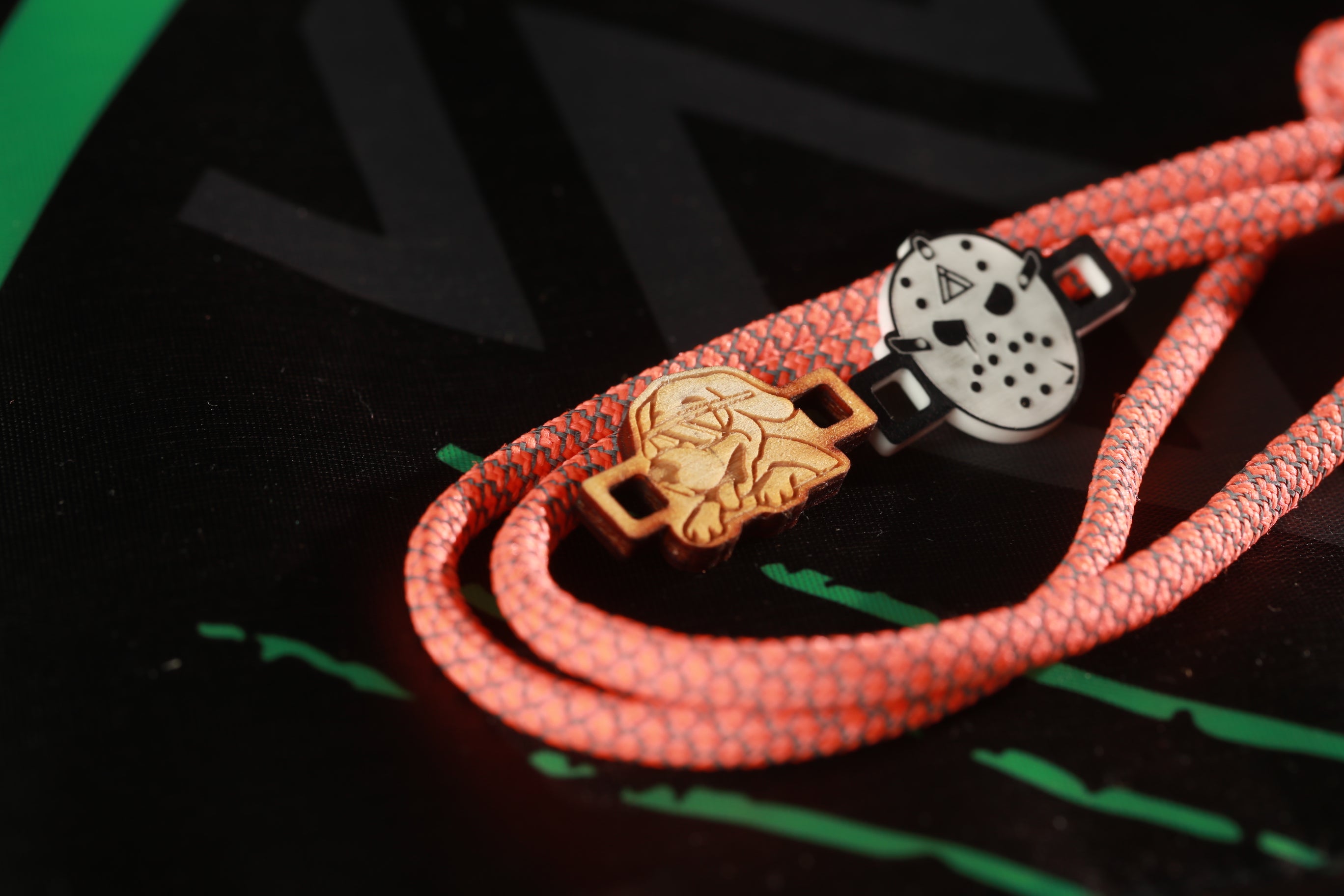a close-up view of a red rope with a wooden charm attached to it, set against a black background with green lines.