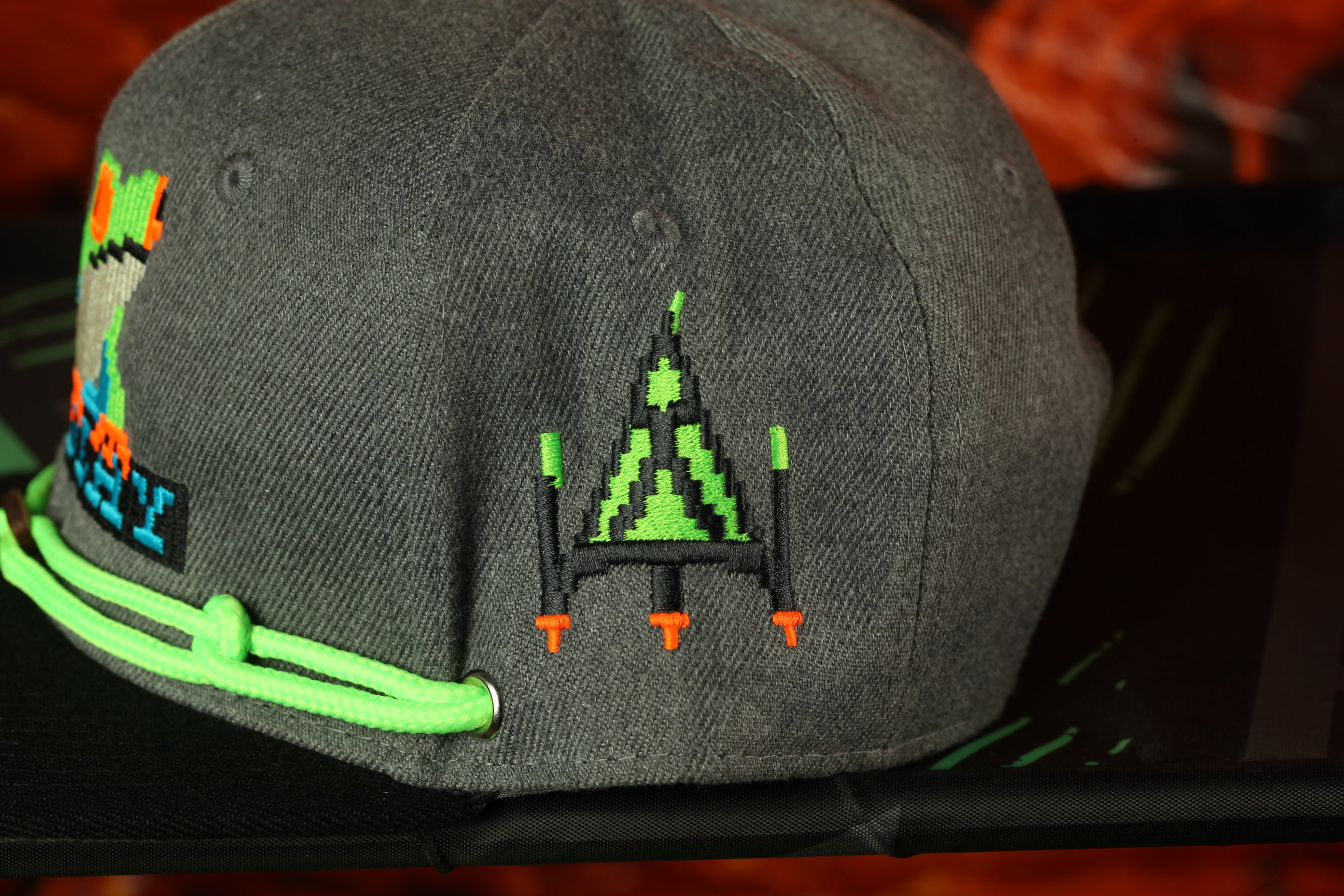 A gray baseball cap with a pixelated design on the front, featuring a green and orange pattern.