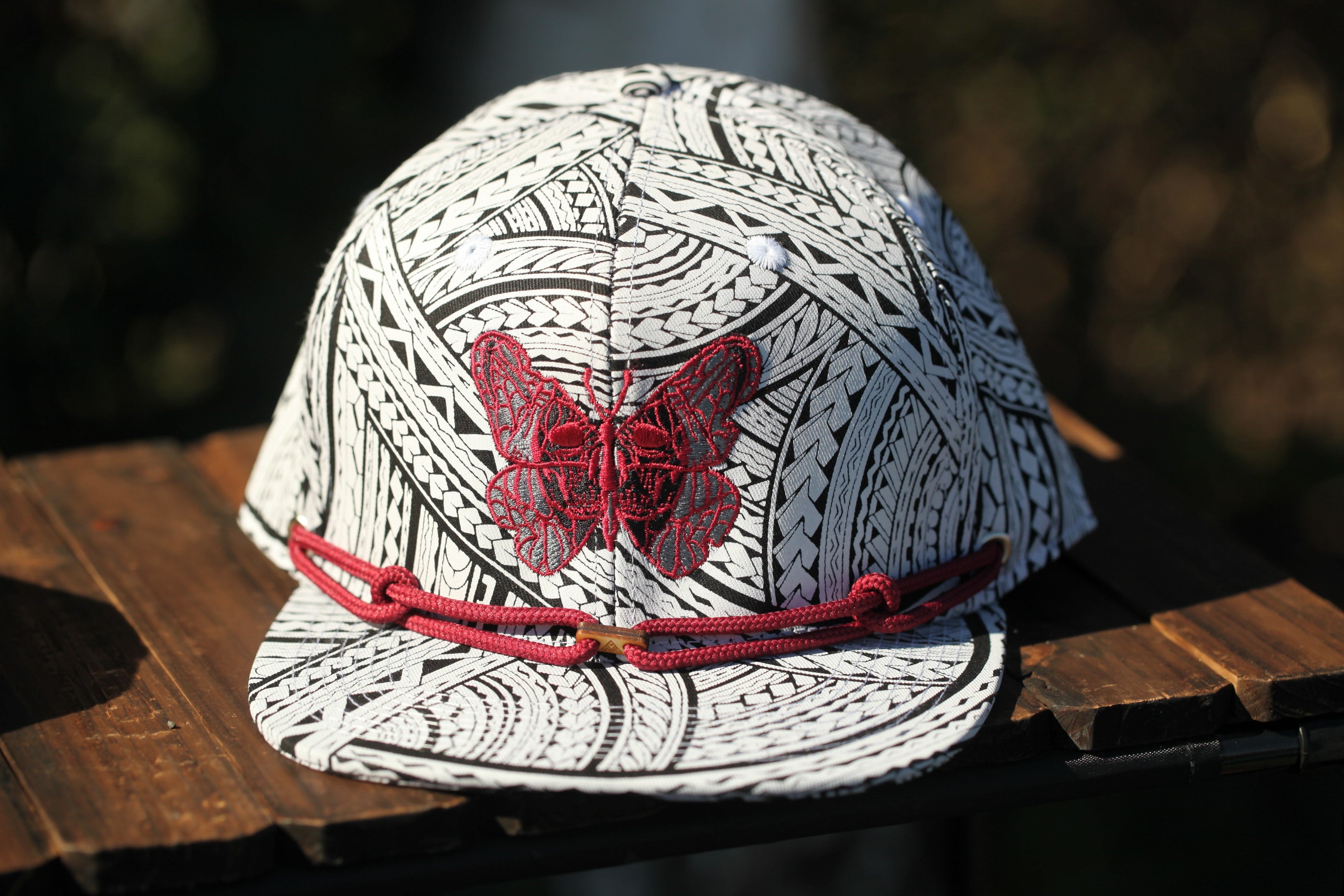 A white baseball cap with a red butterfly embroidered on it, placed on a wooden surface.
