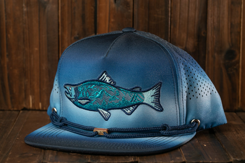 A blue baseball cap with a fish embroidered on it, placed on a wooden surface.