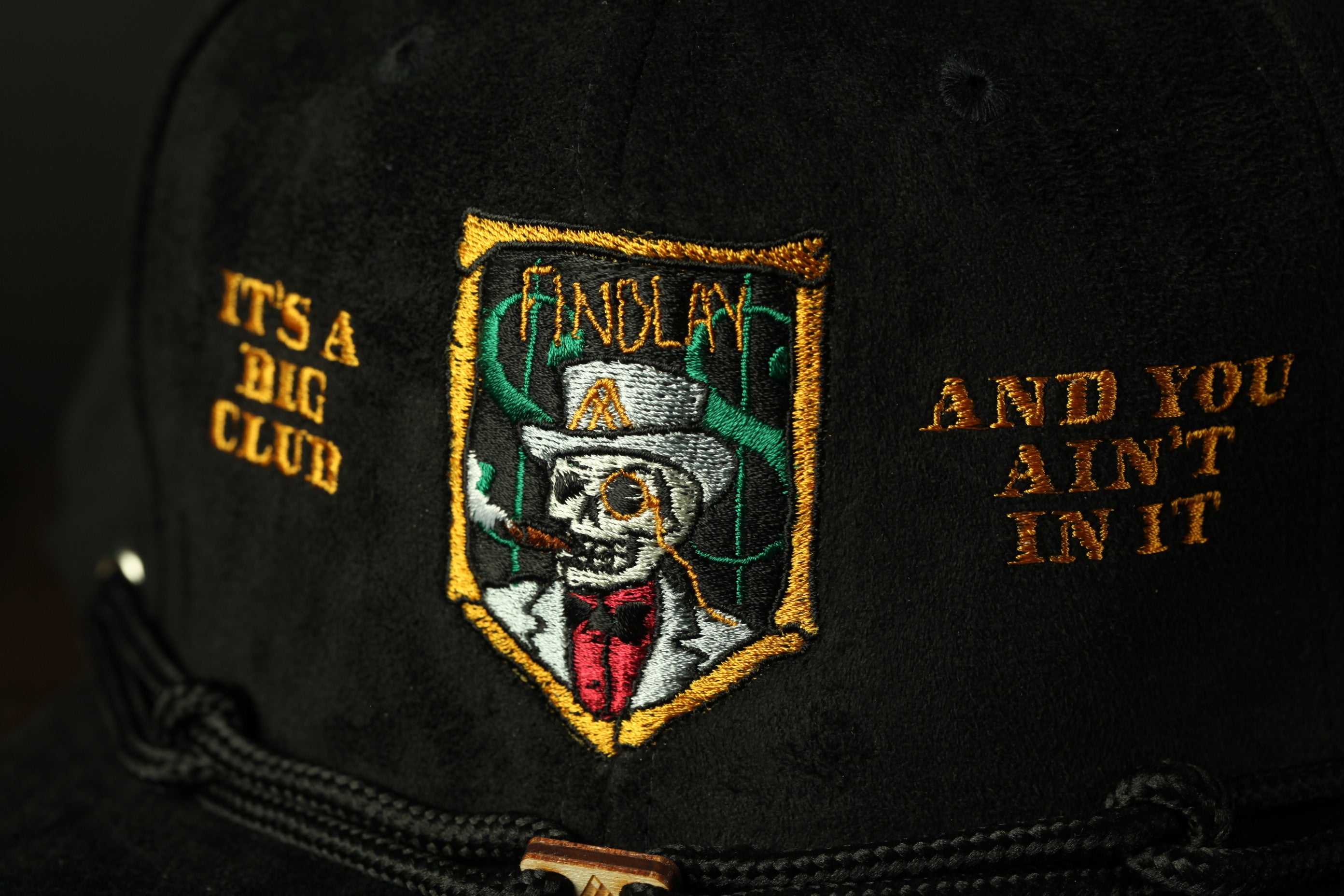 A close-up of a black baseball cap with an embroidered patch featuring a skull wearing a top hat and a red bow tie.