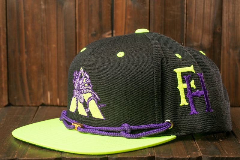 A black baseball cap with purple and yellow accents, including a logo and a string, is displayed on a wooden surface.