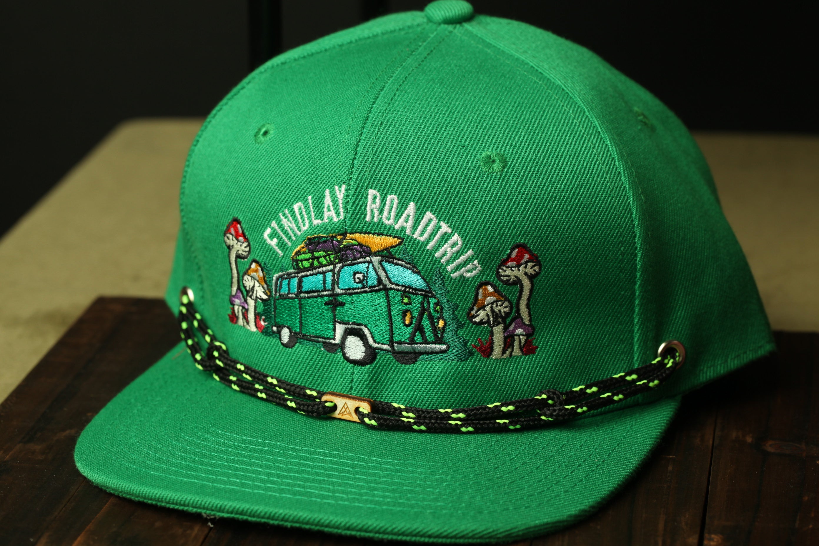 A green baseball cap with an embroidered design on it, featuring a van and mushrooms.