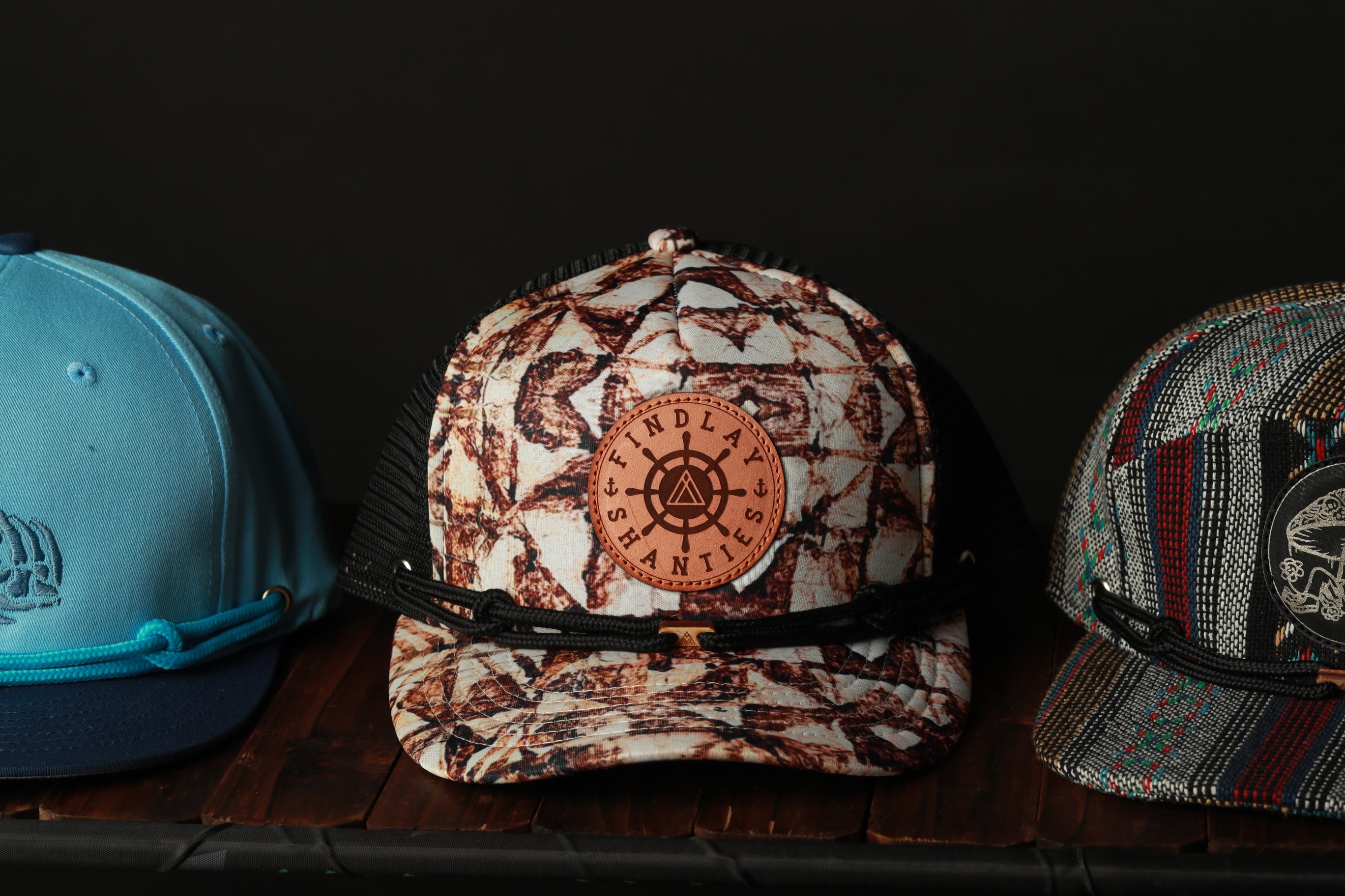 Three baseball caps are displayed on a wooden surface, each with a unique design and color.