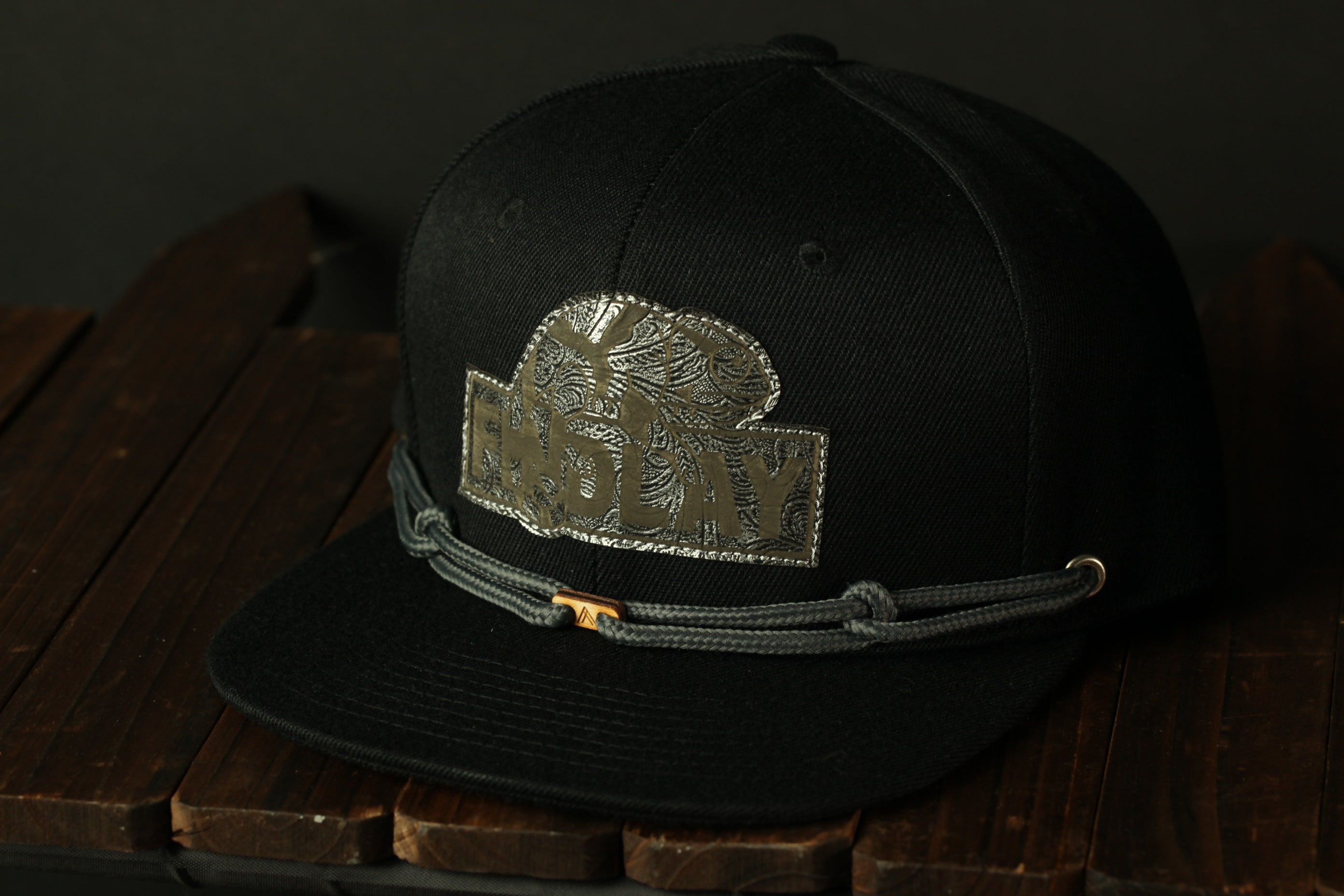 A black baseball cap with a silver logo on the front, resting on a wooden surface.