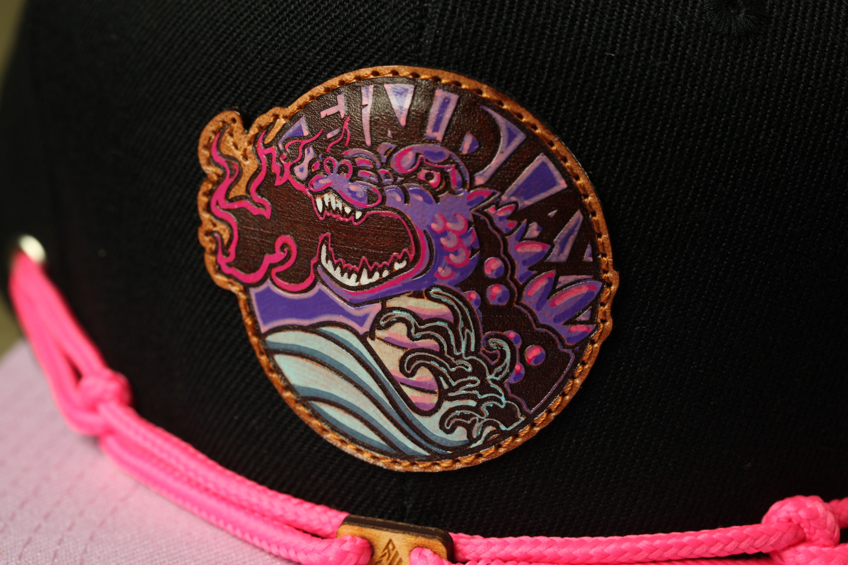 A close-up of a black baseball cap with a colorful, circular patch featuring a dragon-like creature and the word "DUNDY" printed on it.