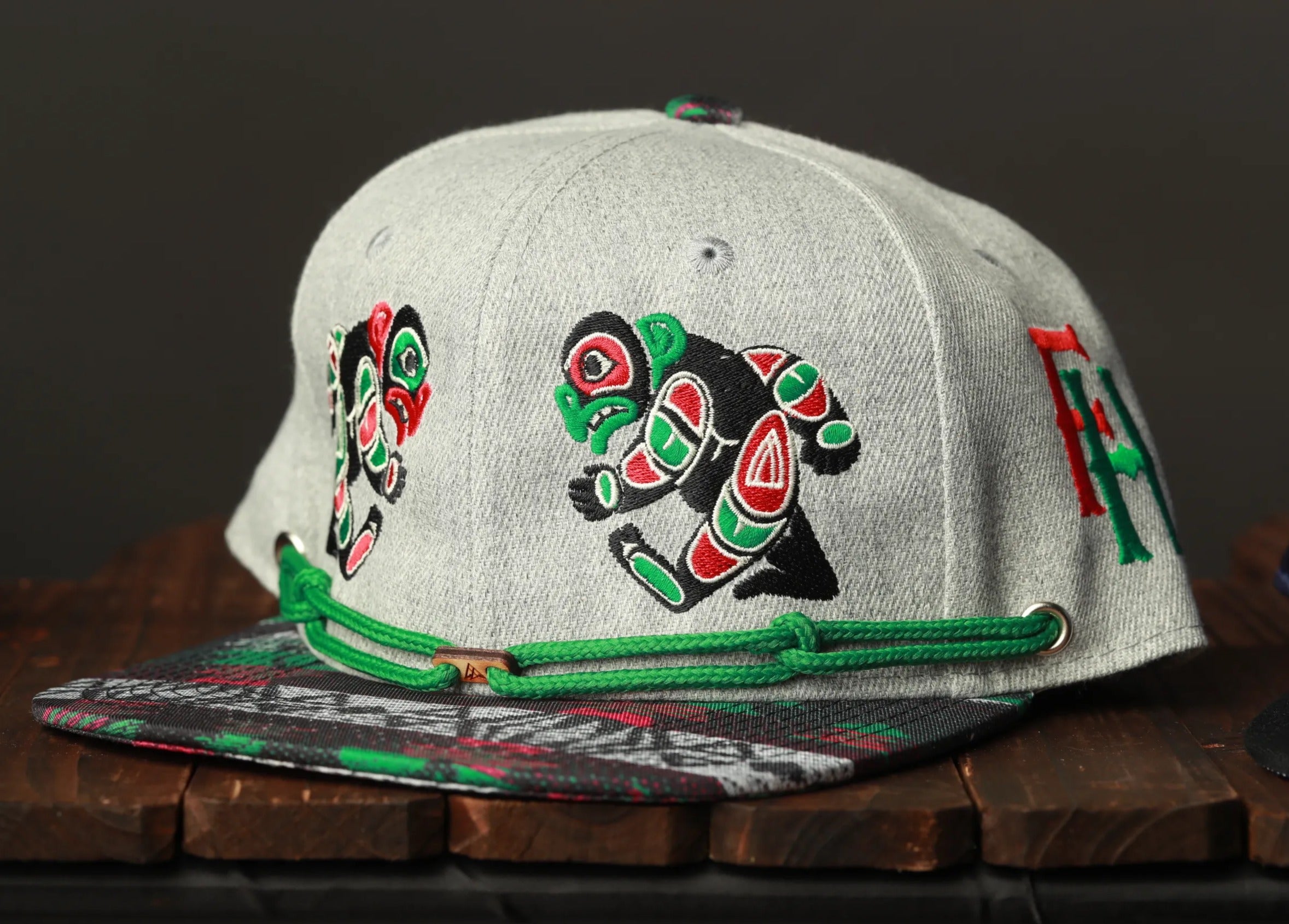 A gray baseball cap with colorful embroidered designs on the front, sitting on a wooden surface.