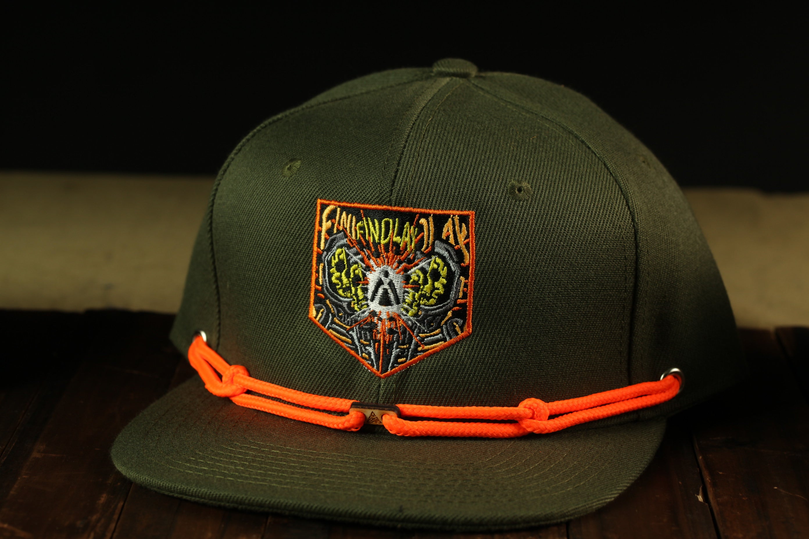 A dark green baseball cap with an orange band and a patch on the front, featuring a colorful design.