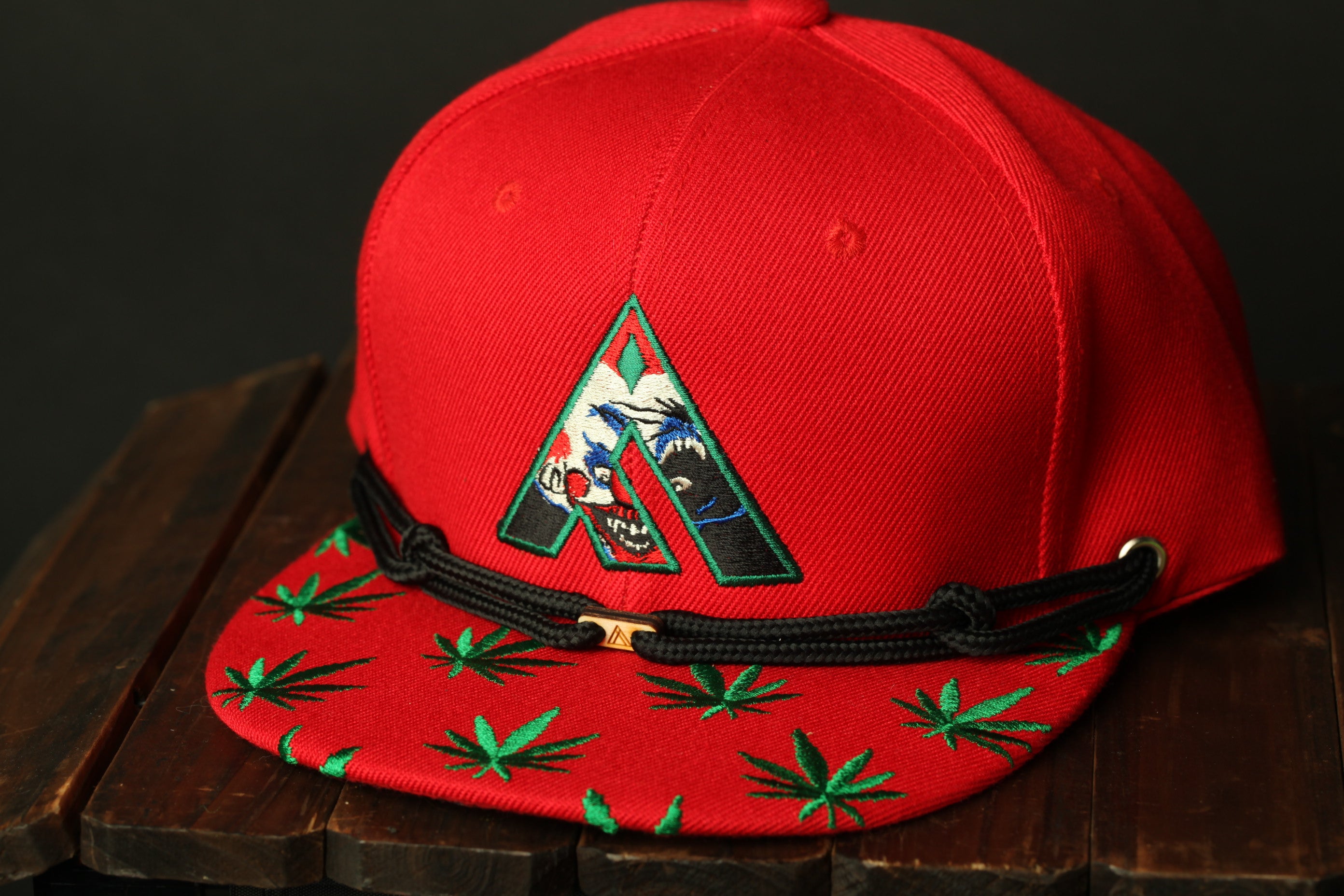 A red baseball cap with a green leaf pattern and a black braided strap.