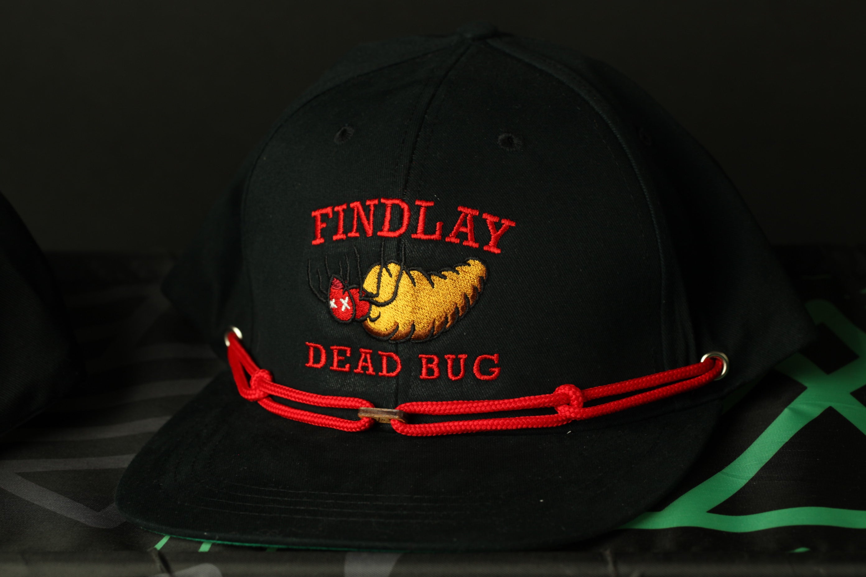 A black baseball cap with a red strap and a logo on it.