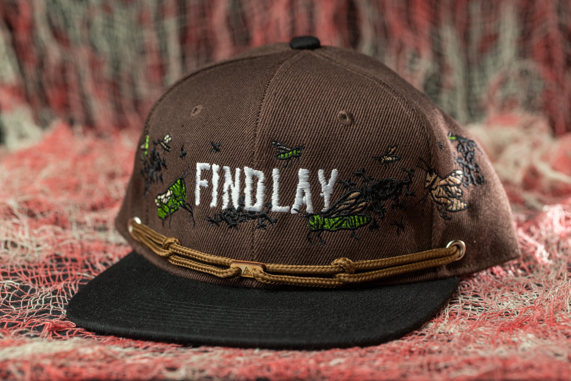 A brown baseball cap with the word "FINDlay" embroidered on it, sitting on a red and white background.