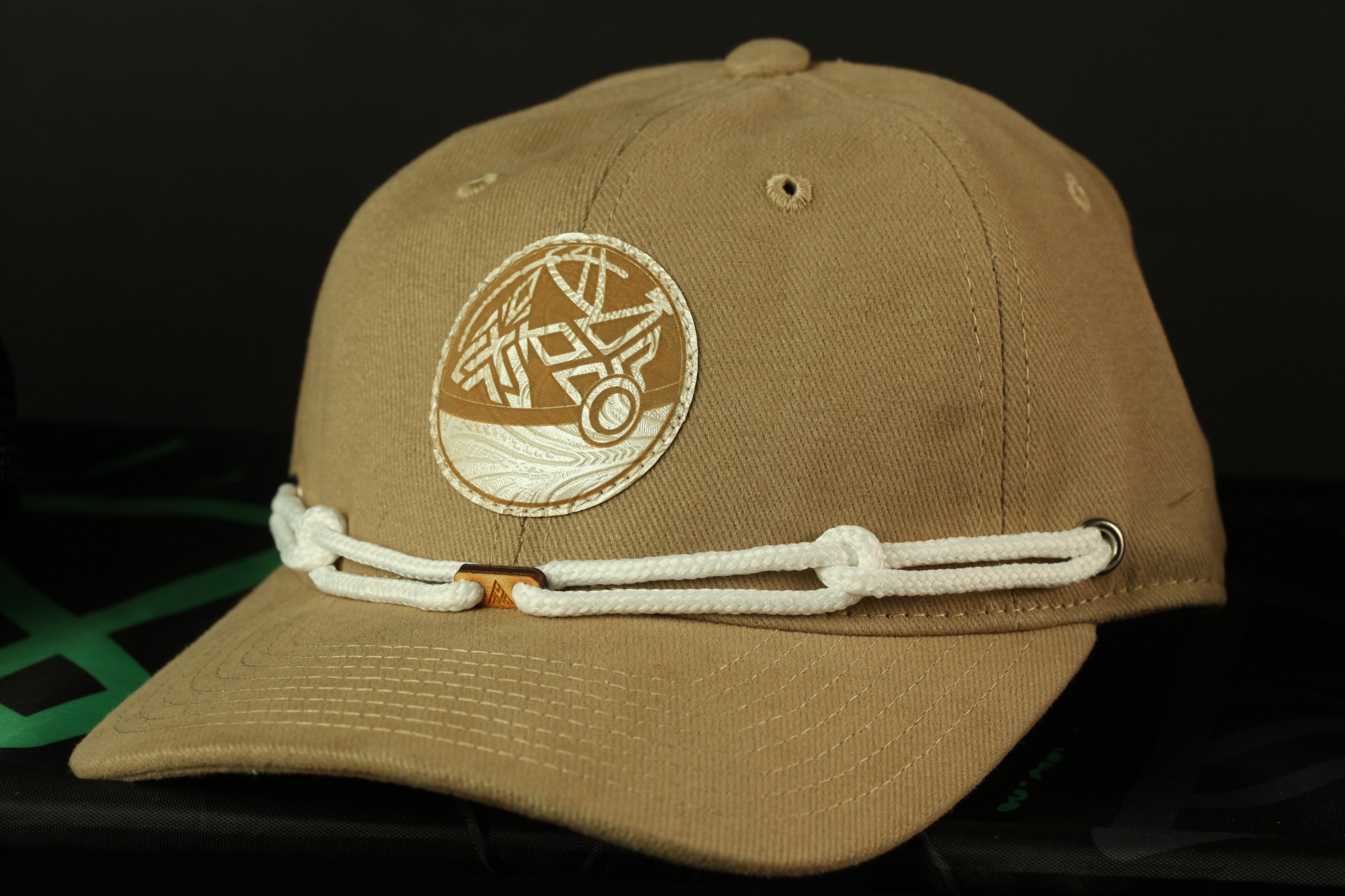 A beige baseball cap with a circular patch on the front, featuring a design, is shown against a dark background.