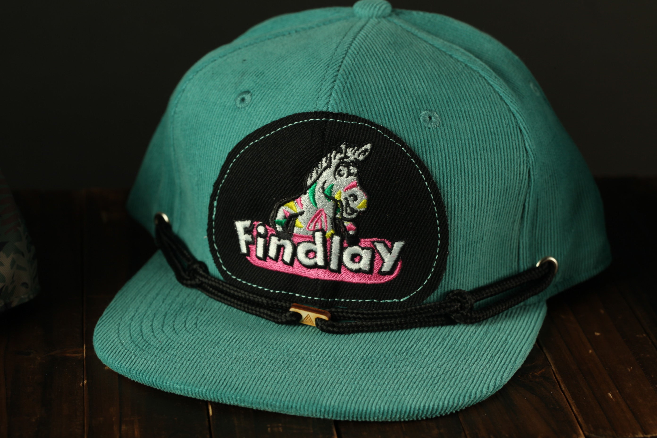 A turquoise baseball cap with a black and pink embroidered patch that says "Findlay" on it.