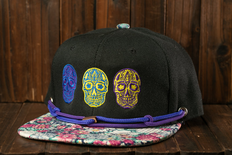 A black baseball cap with colorful skull embroidery on it, placed on a wooden surface.