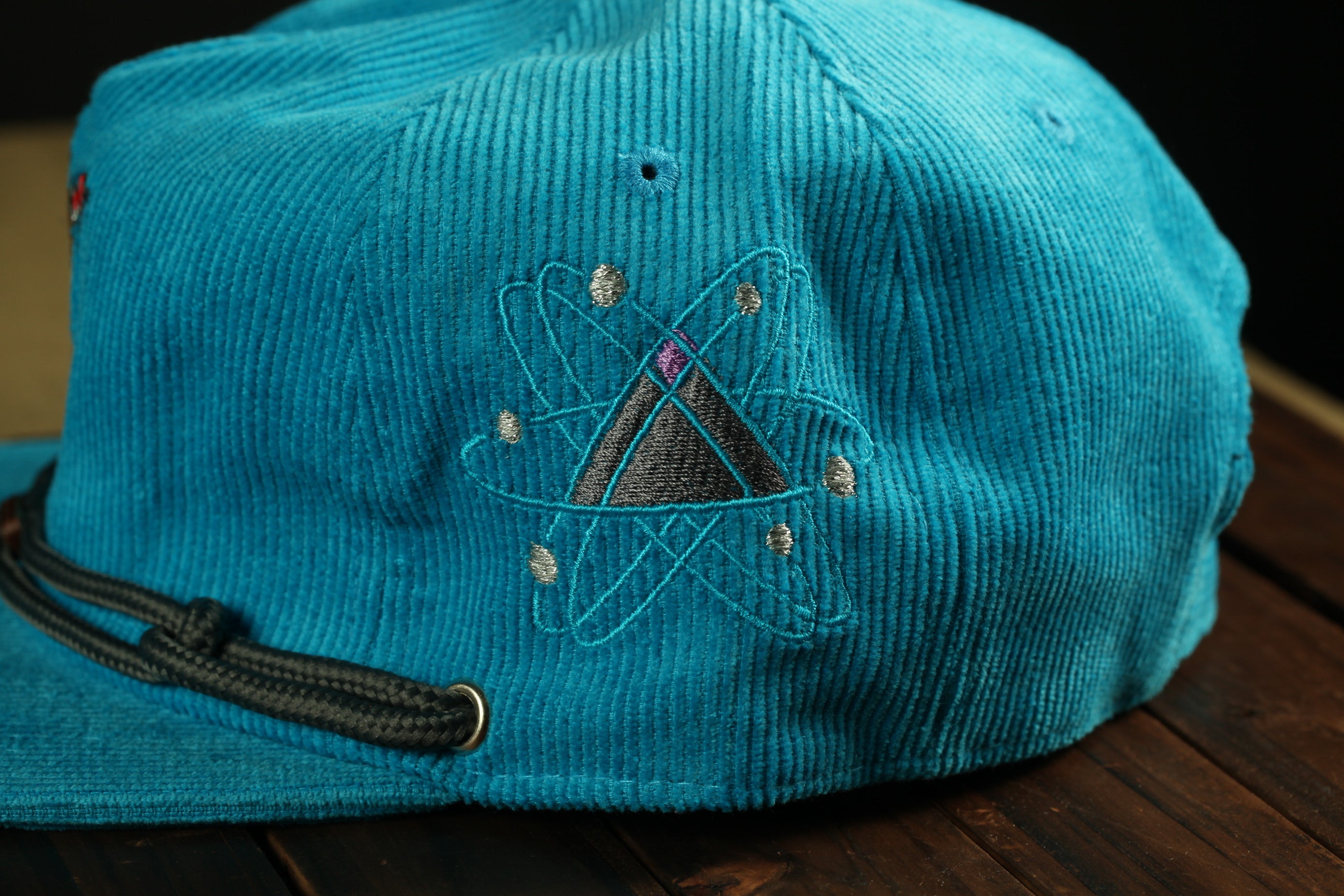 A close-up view of a teal-colored baseball cap with an embroidered design on the front.