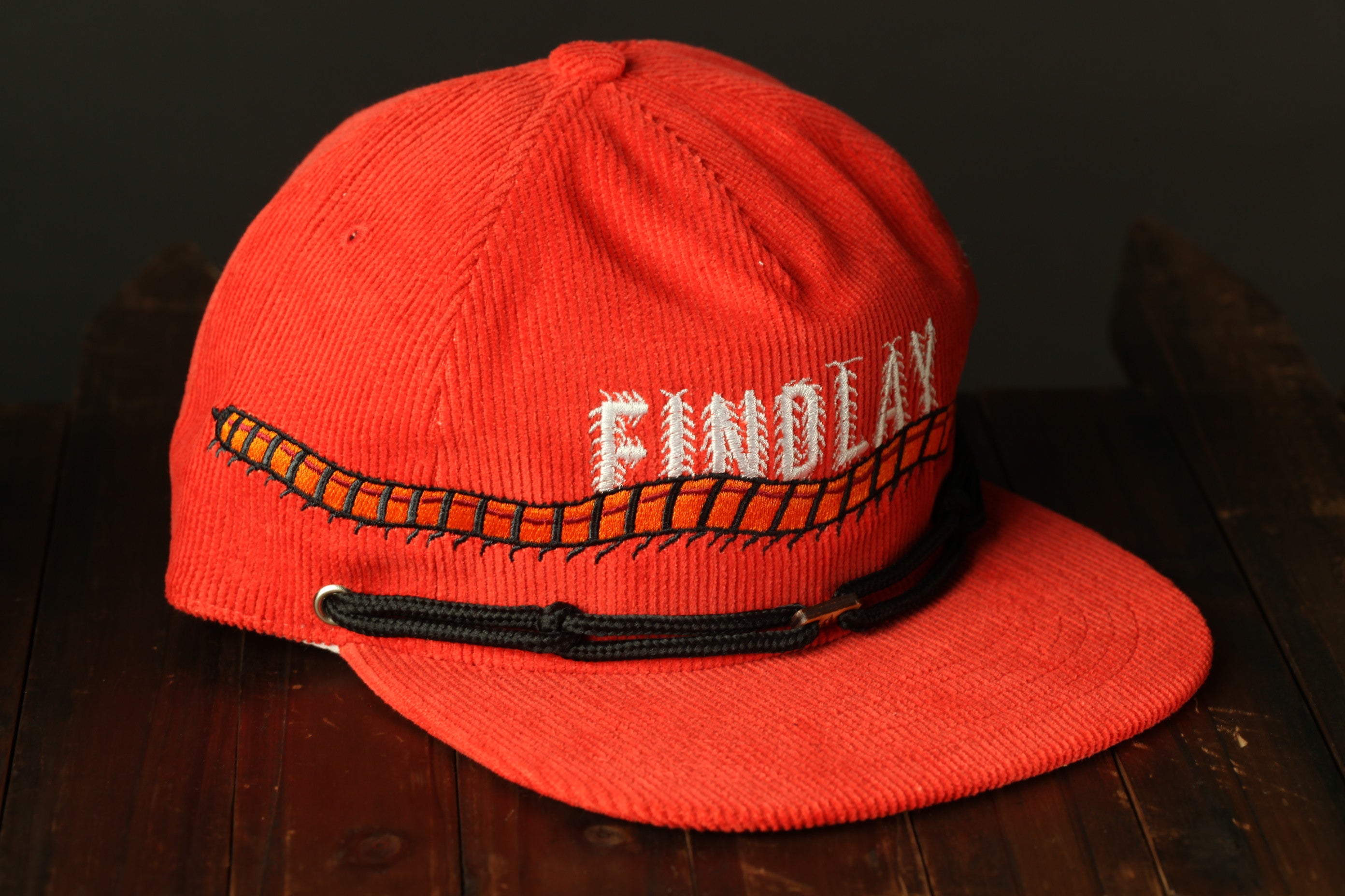 A red baseball cap with the word "FINDLEX" embroidered on it, sitting on a wooden surface.