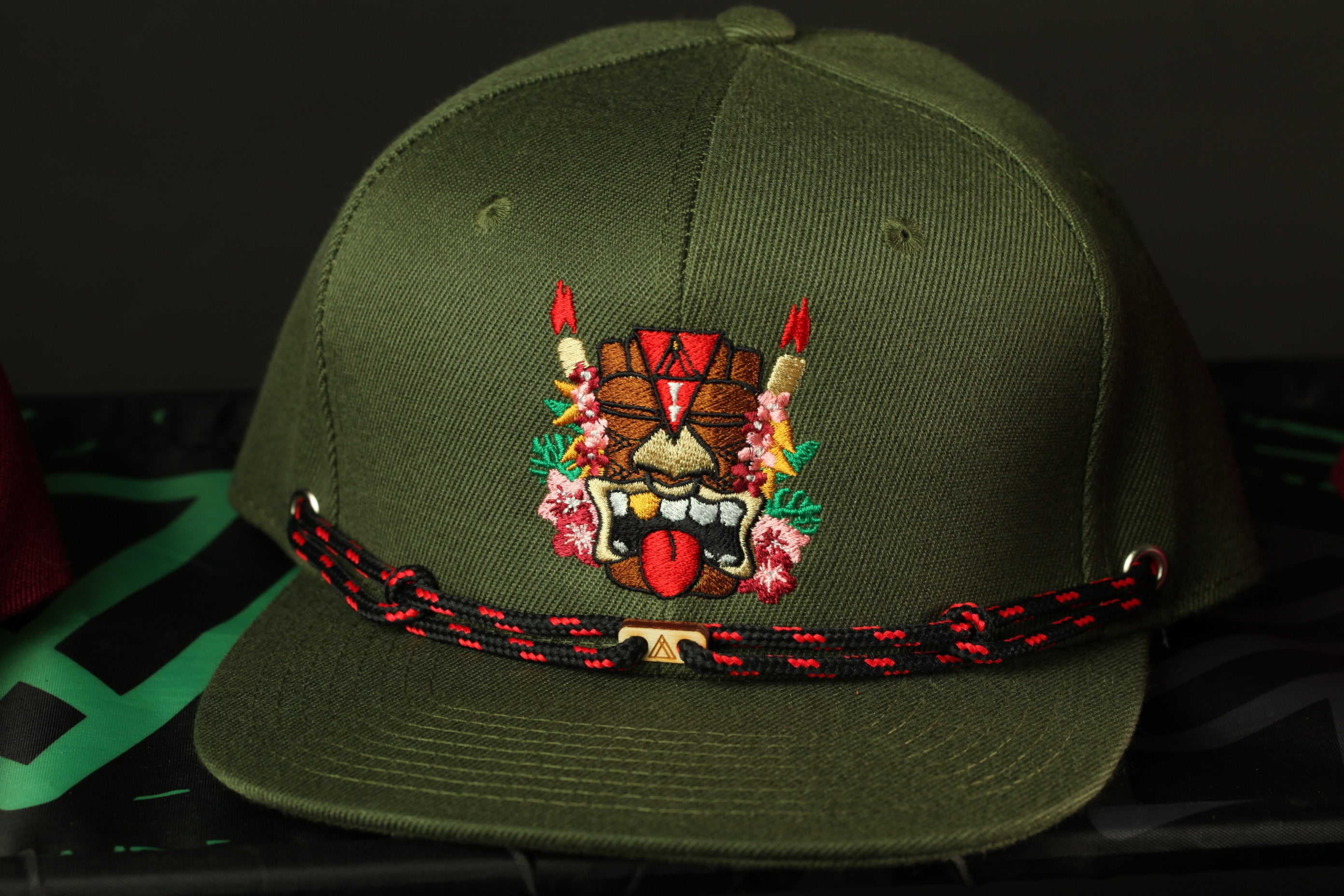 A green baseball cap with a colorful tiki mask design on the front.