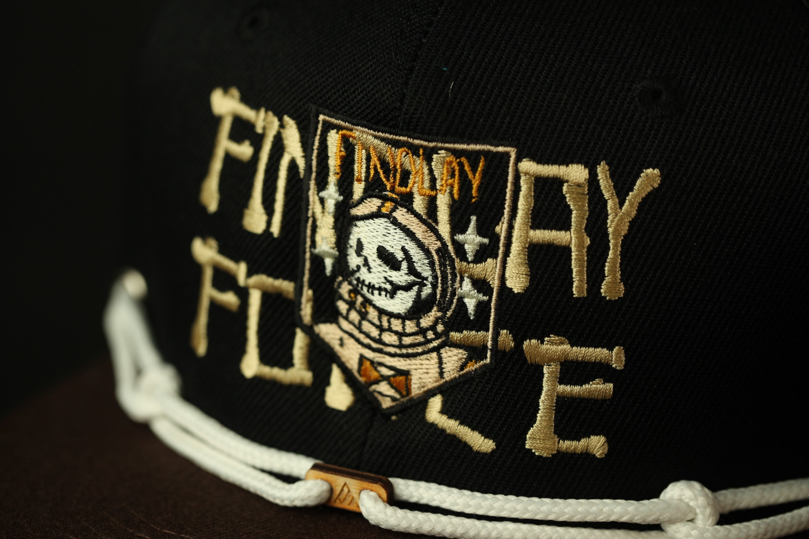 a close-up view of a black baseball cap with gold embroidered text and a graphic design.