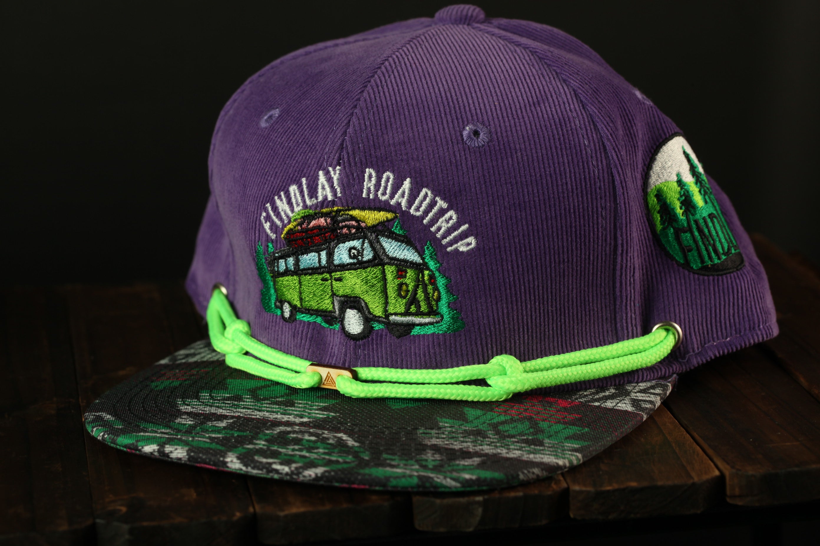 A purple baseball cap with a graphic of a van and the text "FINDLAY ROADTRIP" printed on it.