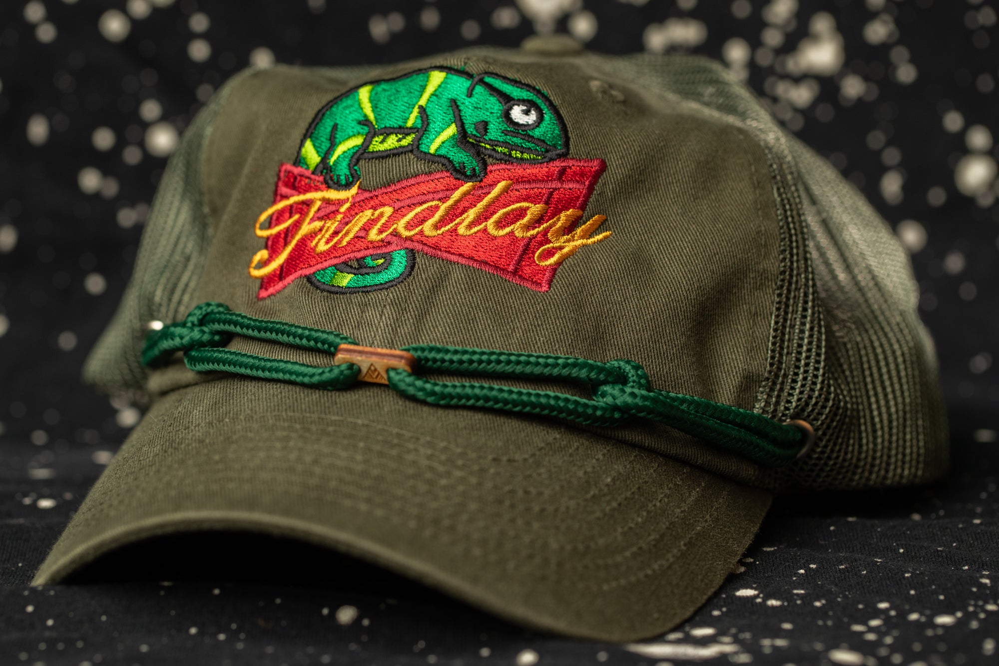 A green baseball cap with a red and yellow chameleon design and the word "Friday" embroidered on it.