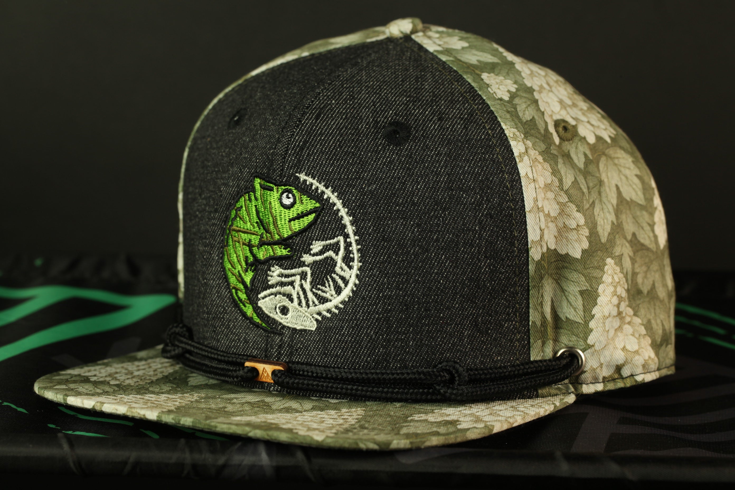 A black and green baseball cap with a chameleon design on the front.