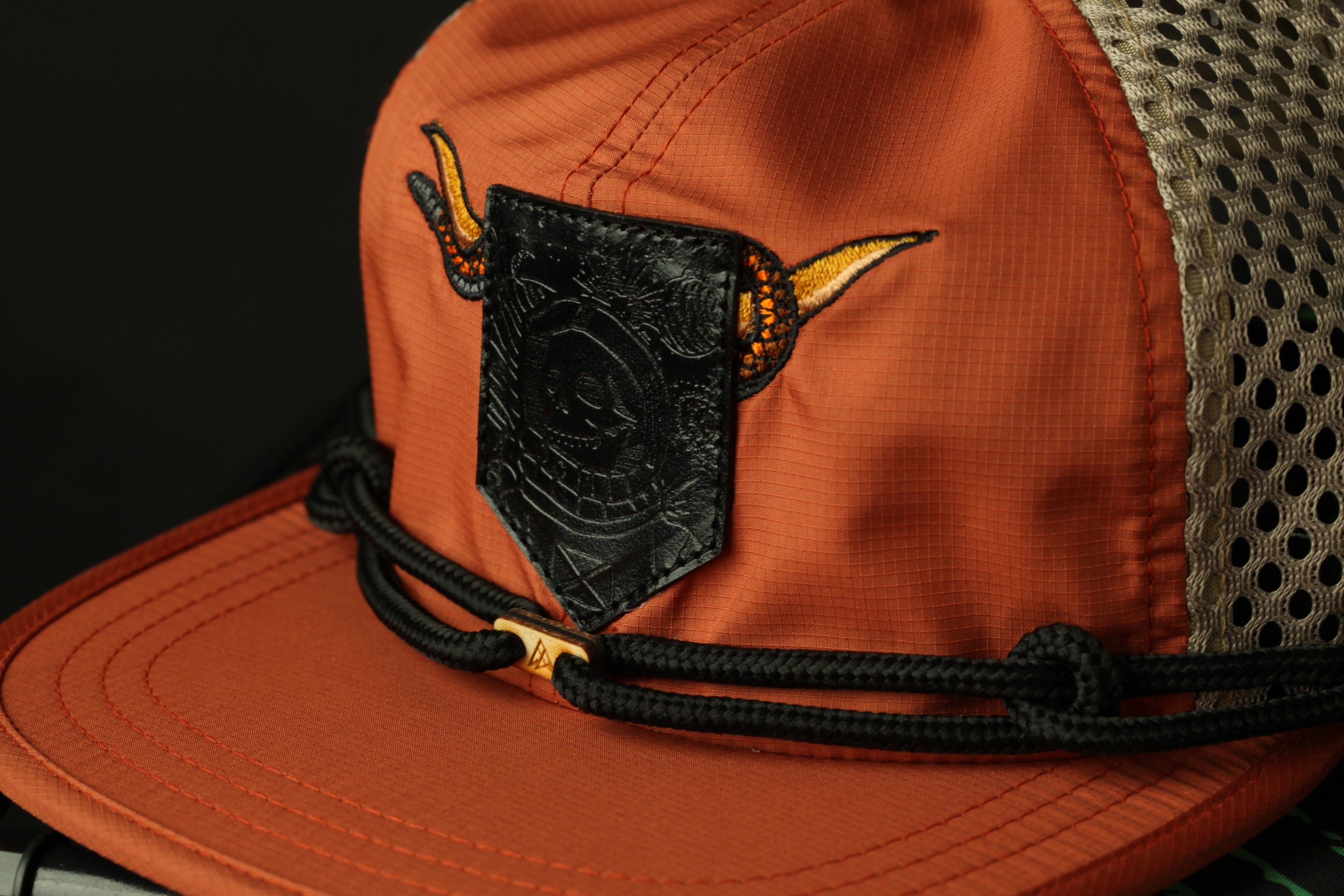 A close-up view of an orange baseball cap with a black patch featuring a logo and a pair of horns.