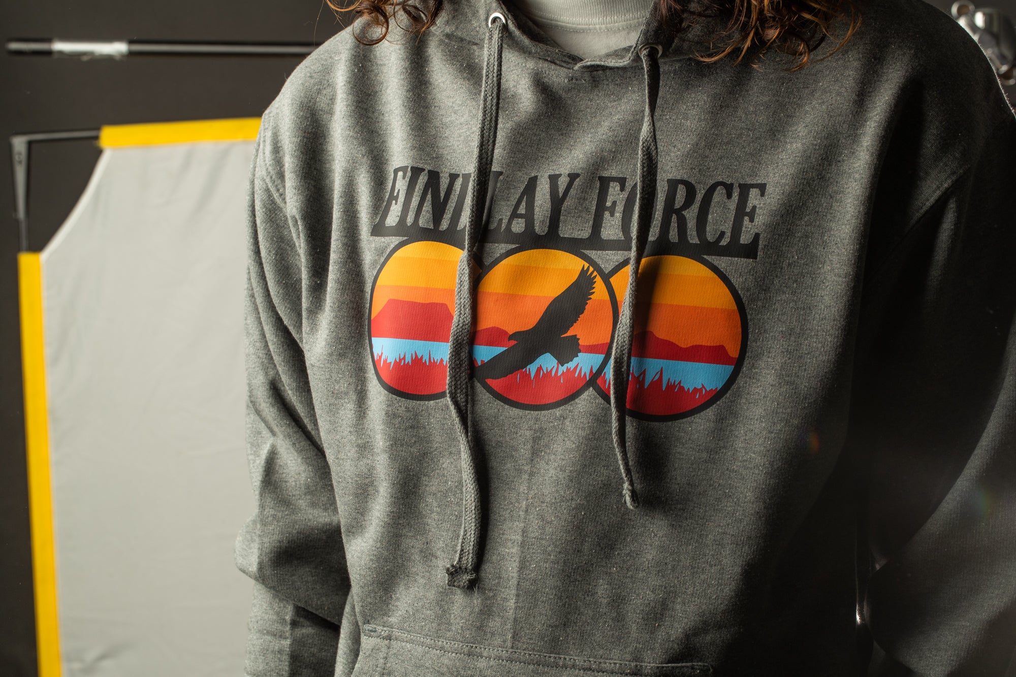 A person wearing a grey hoodie with a graphic design featuring a bird and a sunset.