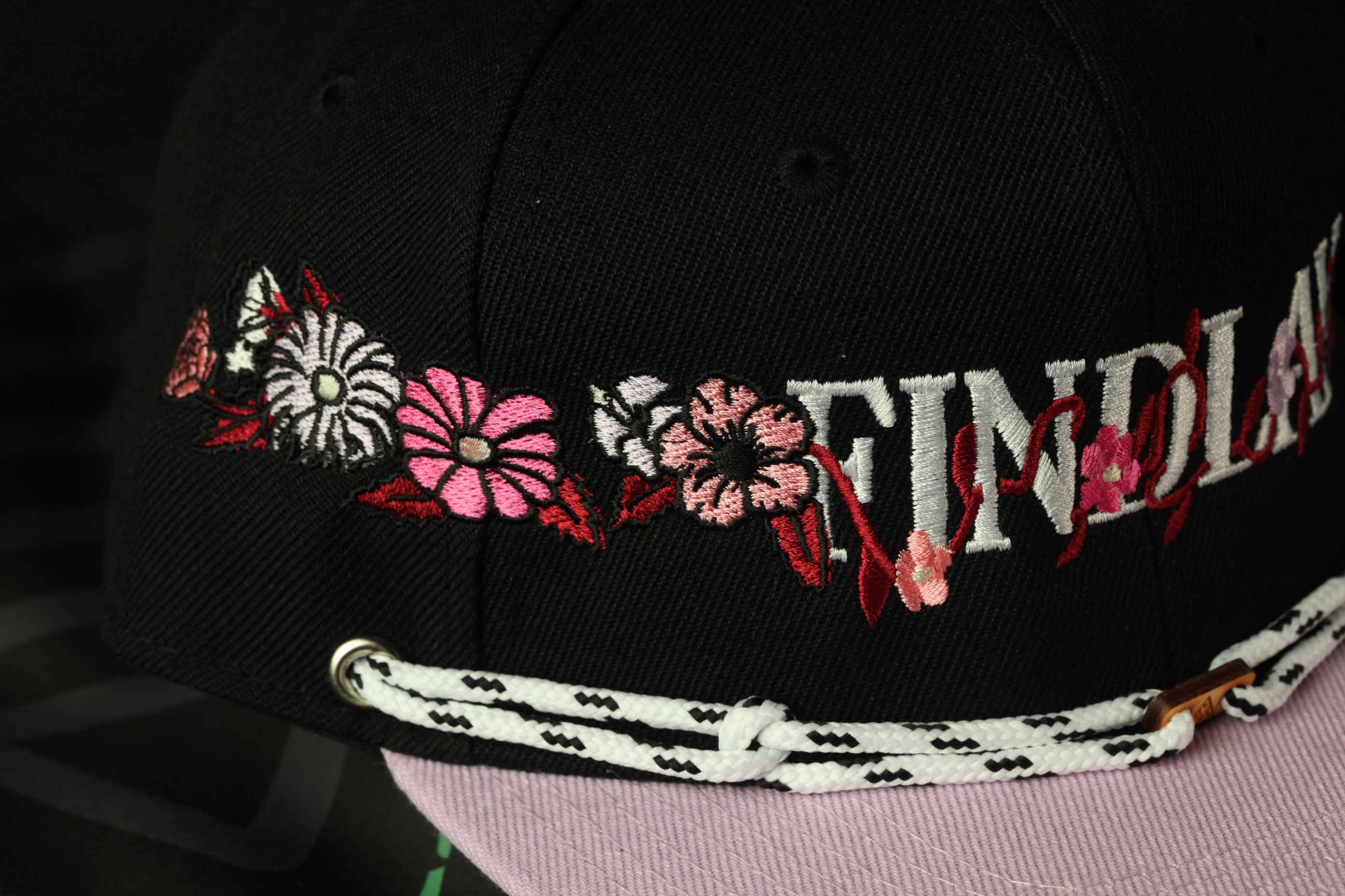 A close-up view of a black baseball cap with colorful floral embroidery and a white lace strap.