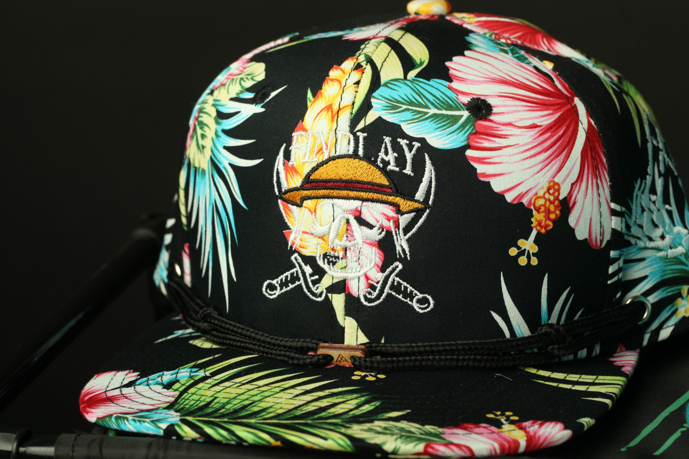 A colorful floral-patterned baseball cap with a pirate-themed logo.