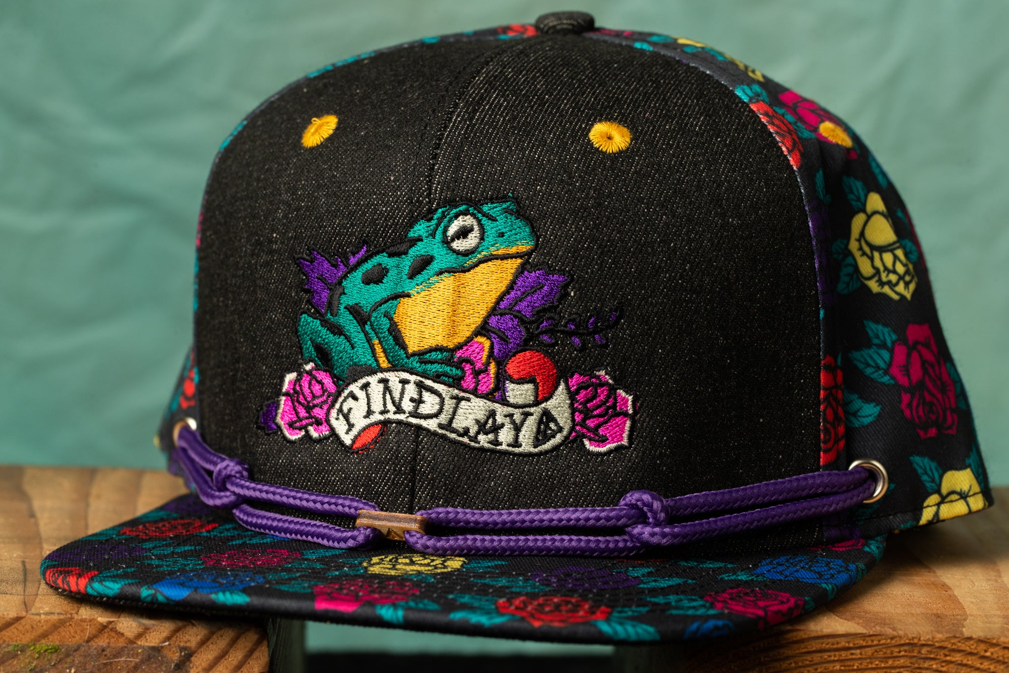 A colorful baseball cap with a frog design and the text "FIND MY" printed on it.