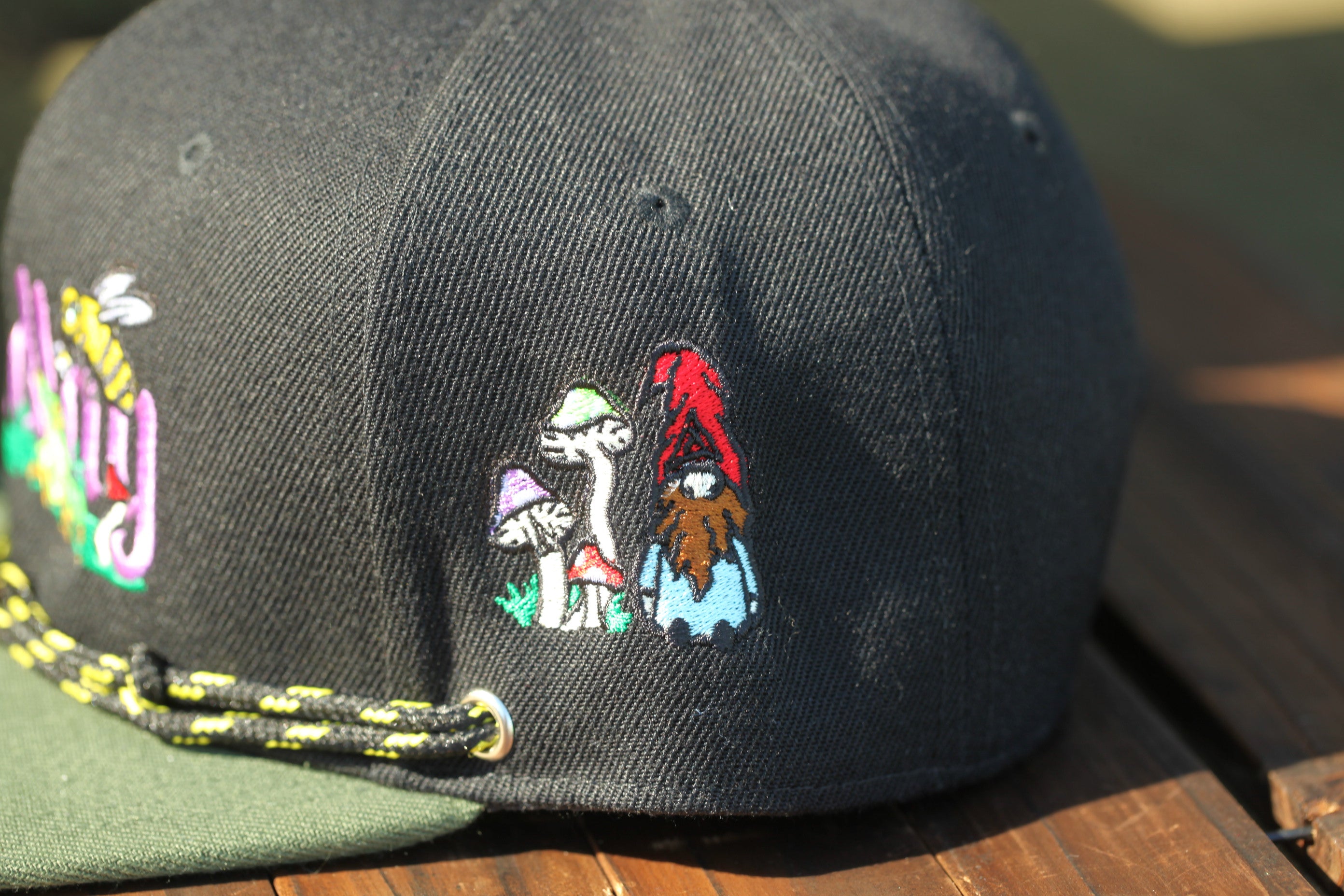 A close-up view of a black baseball cap with colorful embroidered designs, including mushrooms and other whimsical characters.