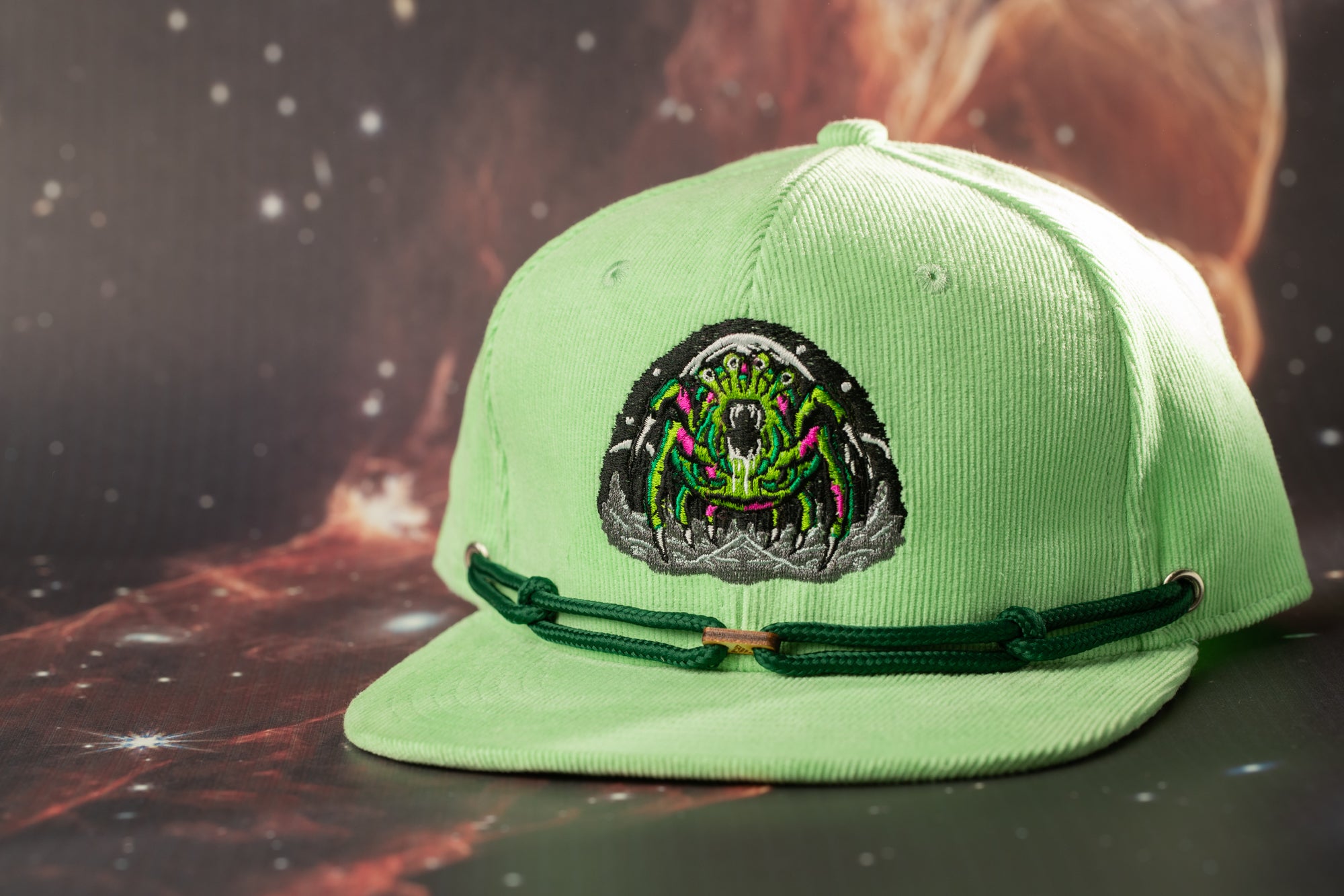 A green baseball cap with a unique embroidered design on the front, featuring a green and black insect-like creature.