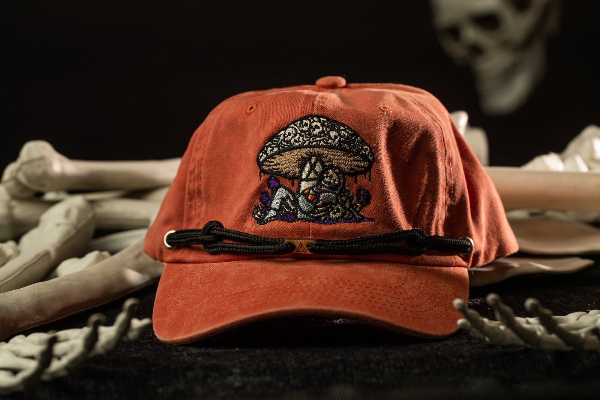 An orange baseball cap with a mushroom design sits on a surface surrounded by skeletal bones.