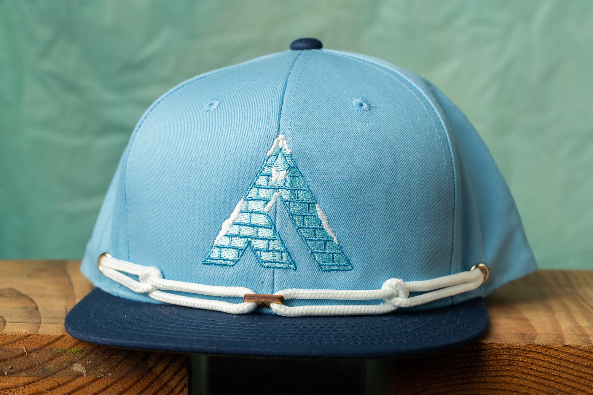A blue baseball cap with a white rope strap and a logo on the front, placed on a wooden surface.