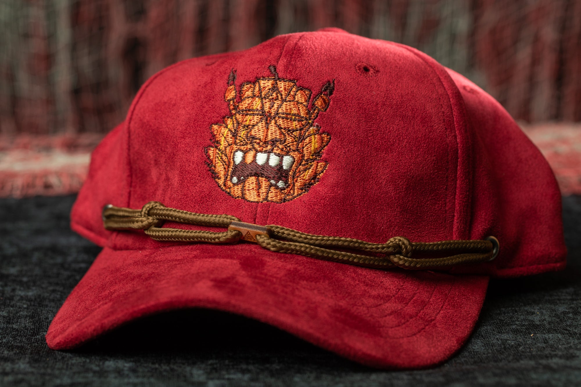 A red baseball cap with a brown leather strap and an embroidered design on the front.