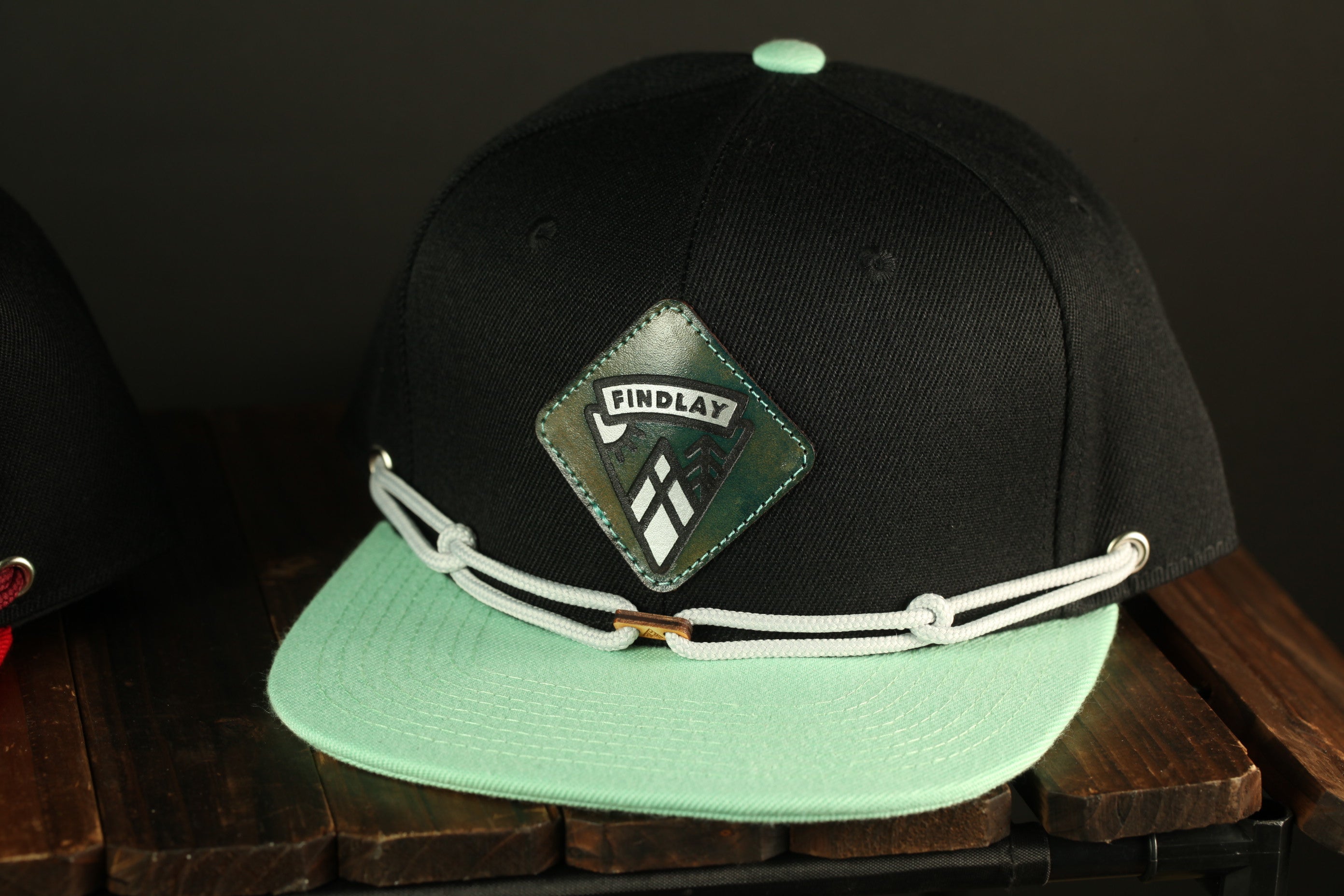 A black baseball cap with a mint green brim and a white string, featuring a logo on the front.