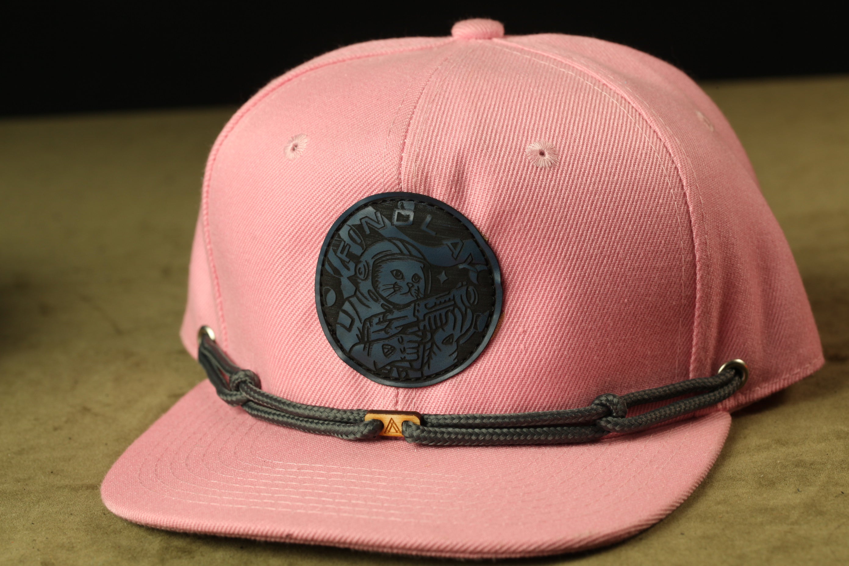 A pink baseball cap with a black circular patch featuring a cartoon character on it.