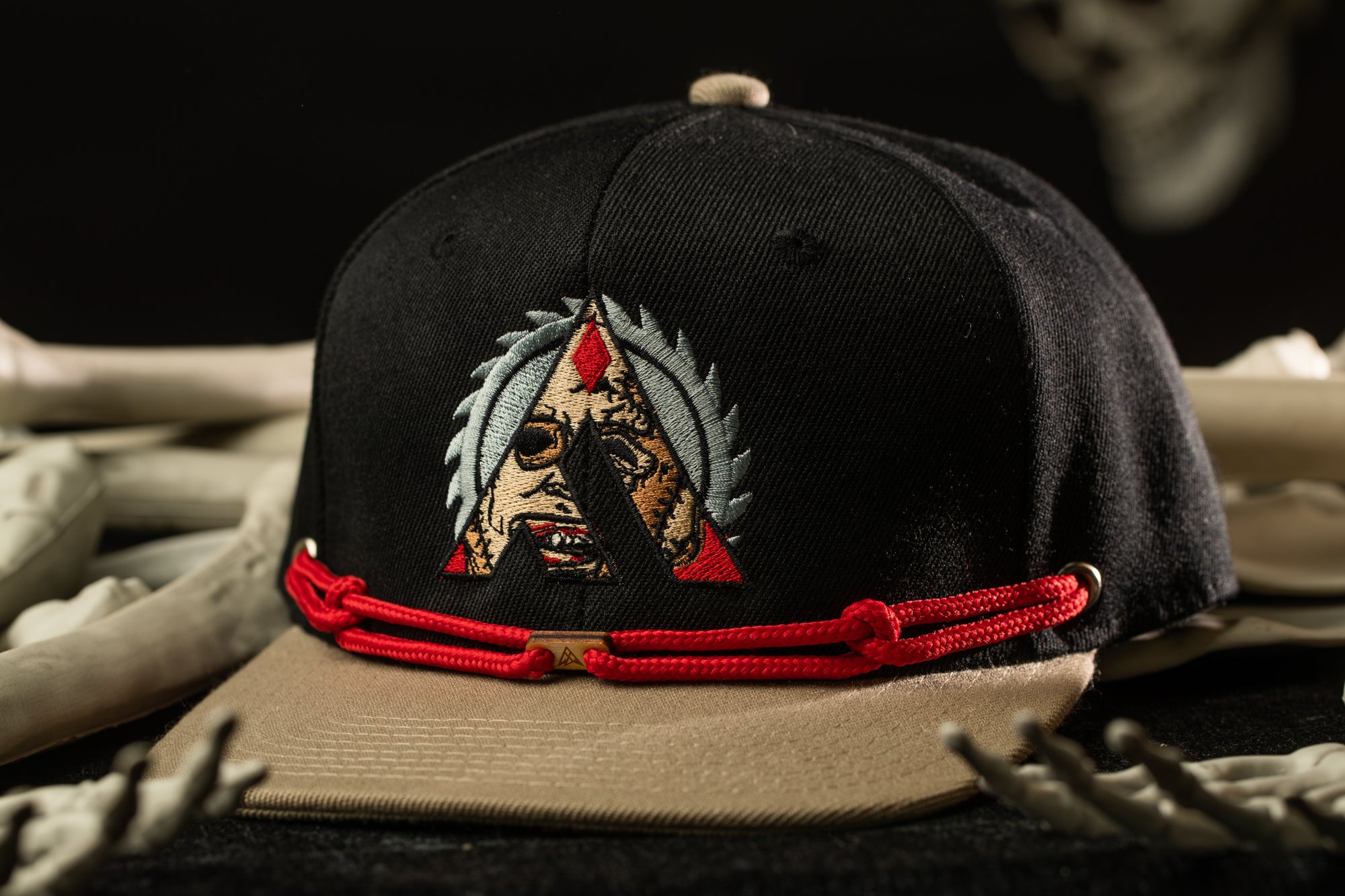 A black baseball cap with a red and gold embroidered design on the front, featuring a stylized face with a triangular shape above it.