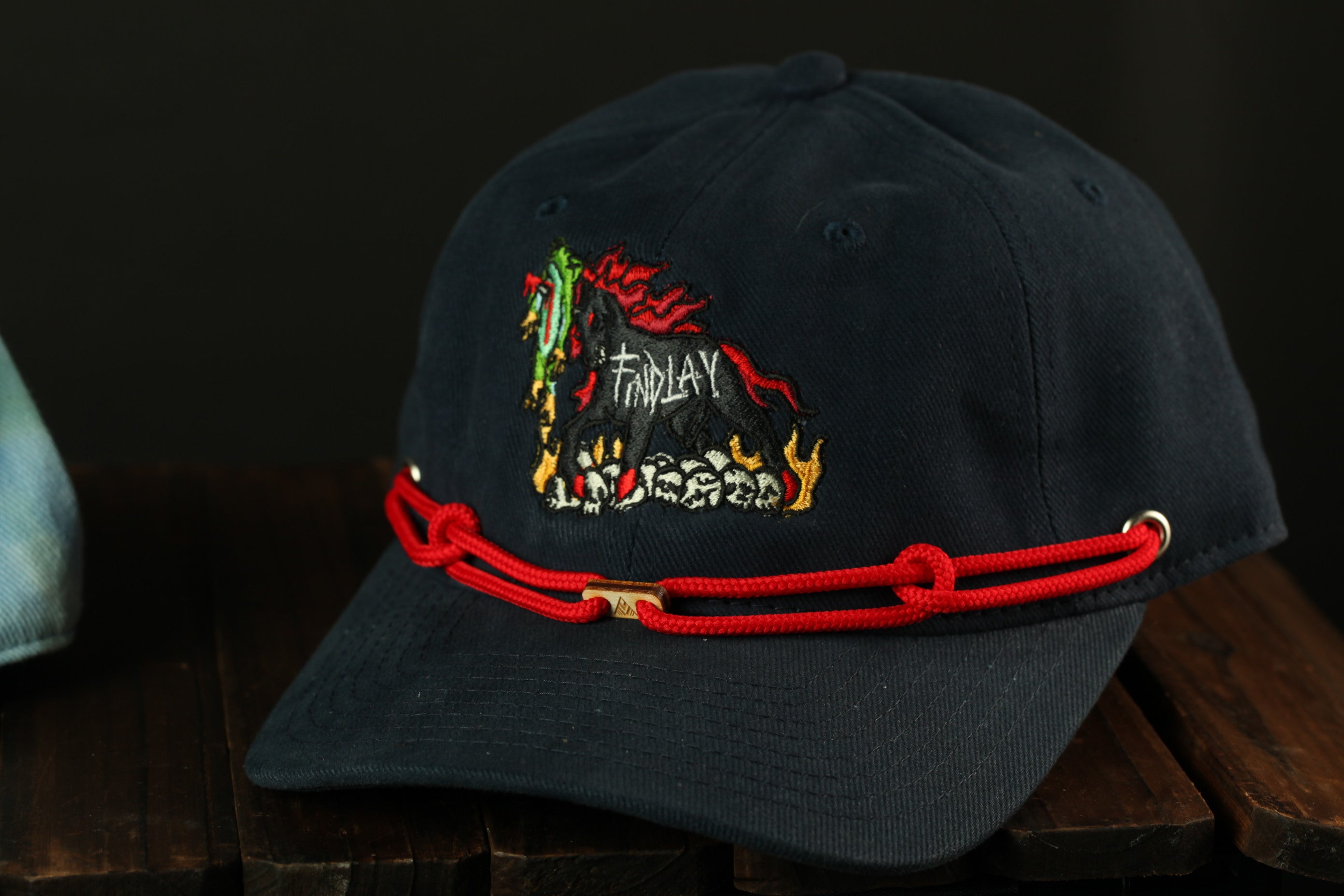 A navy blue baseball cap with a red string and a colorful embroidered design on the front.