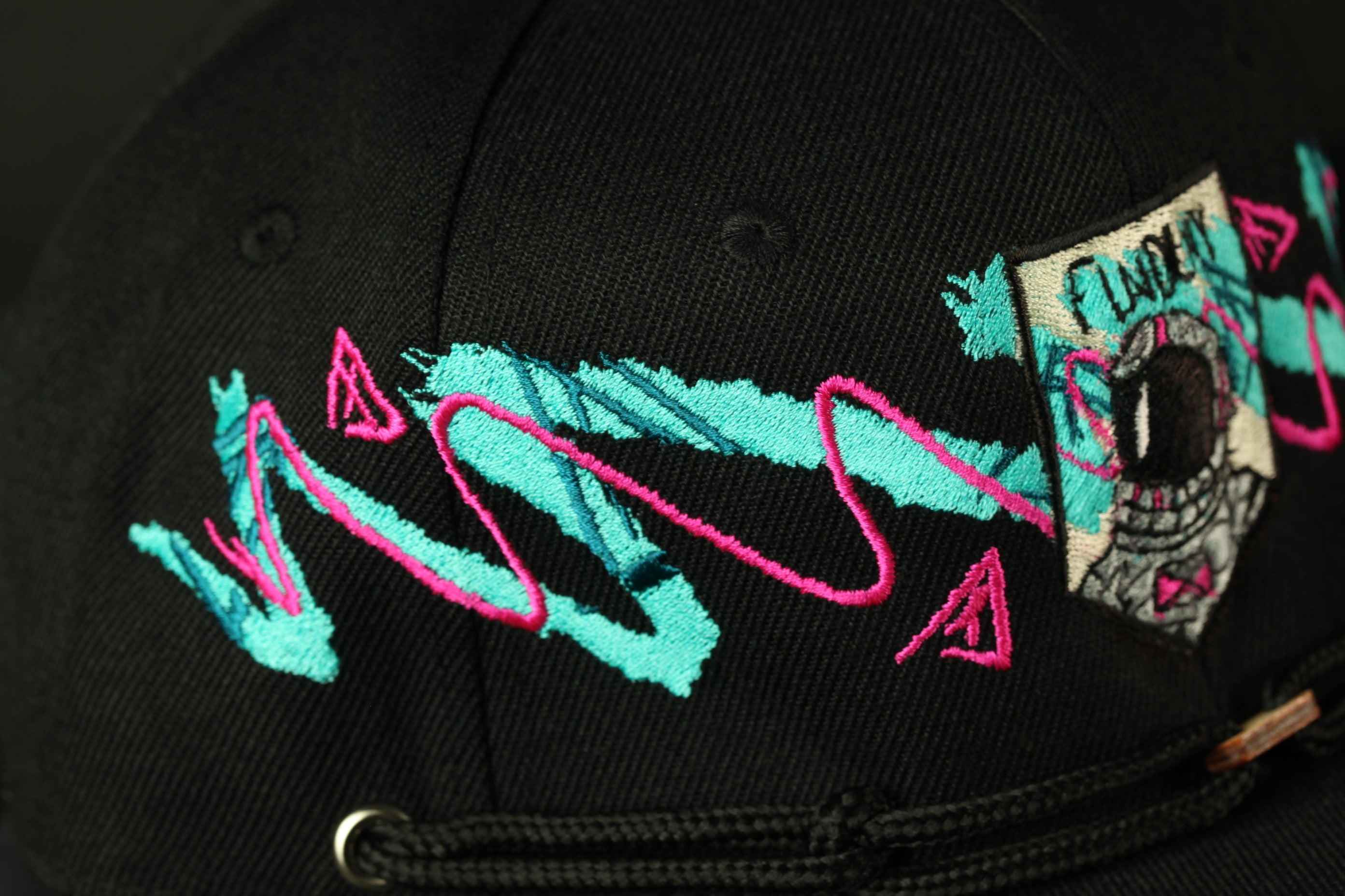 a close-up view of a black baseball cap with colorful embroidered designs, including a patch and a wave-like pattern.