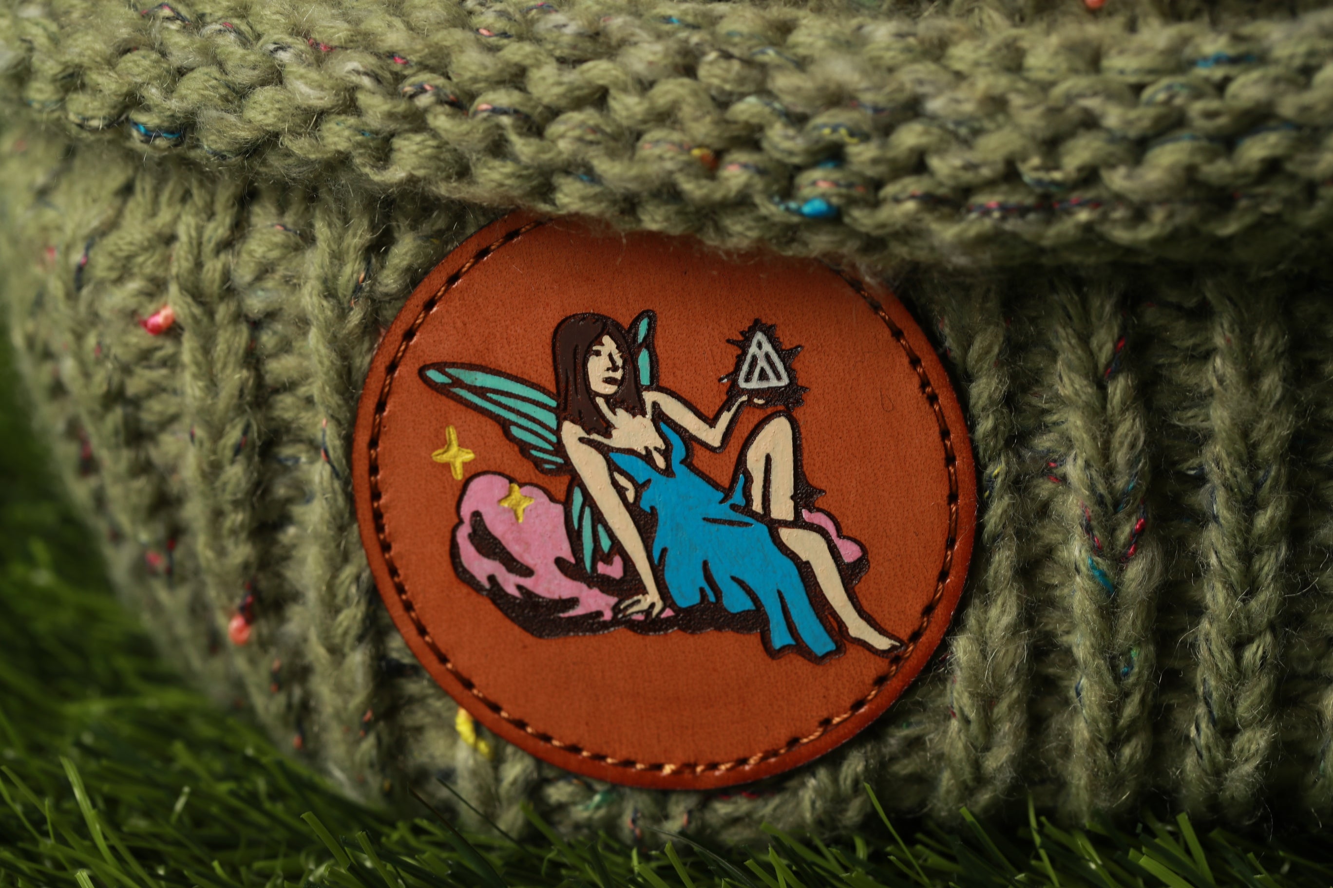 A circular patch with a fairy-like figure holding a triangle, surrounded by a green, knitted fabric.