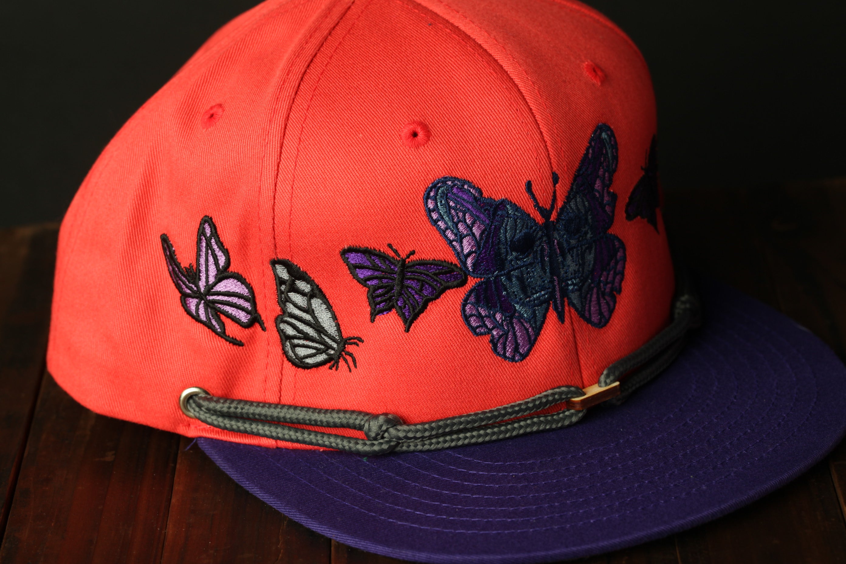 A red baseball cap with a purple and black butterfly design on it.