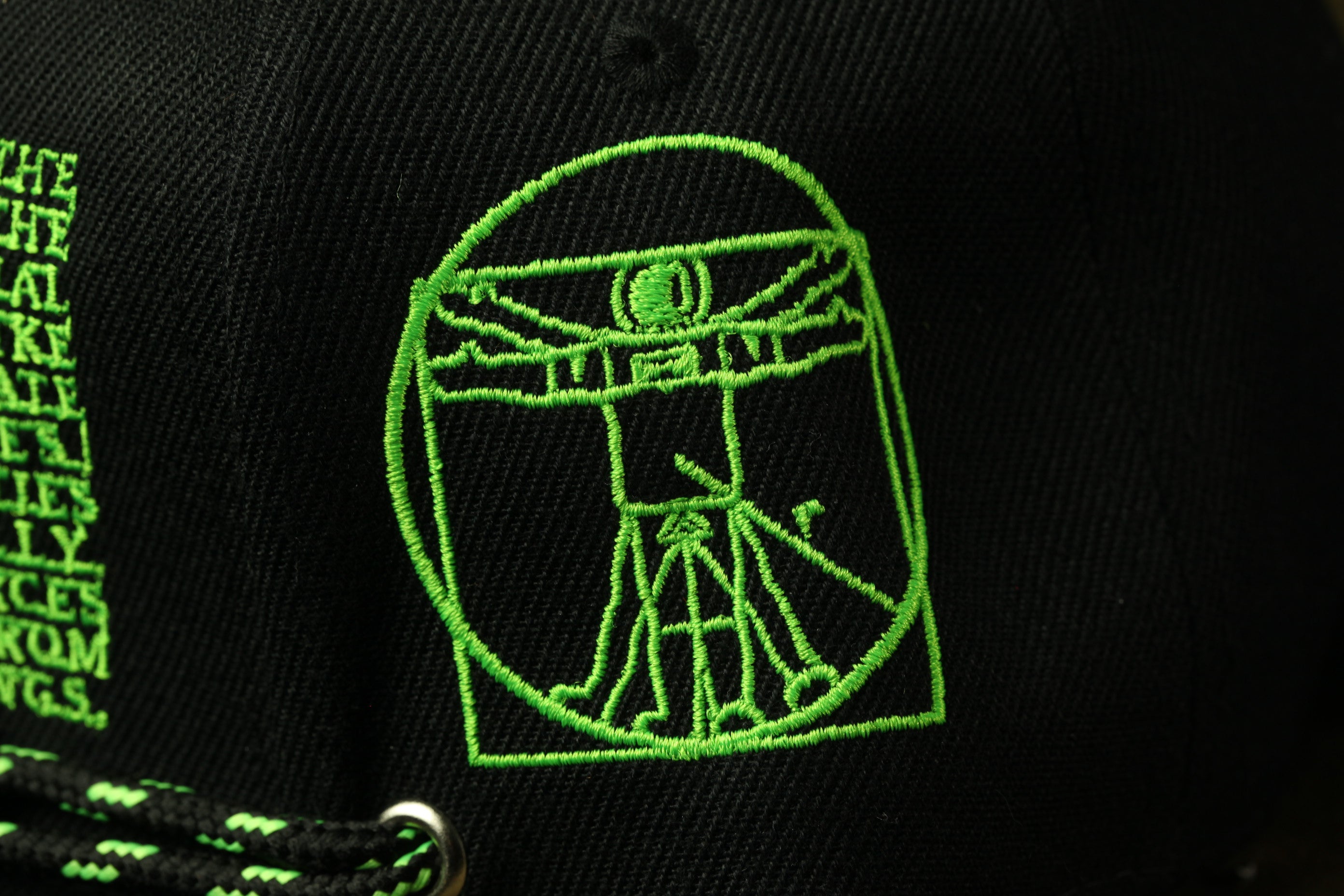 a close-up view of a black fabric with a green embroidered figure, resembling a stylized human or animal.