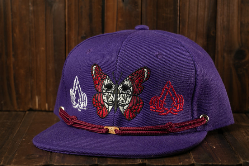 A purple baseball cap with a butterfly design and other embroidered patterns.